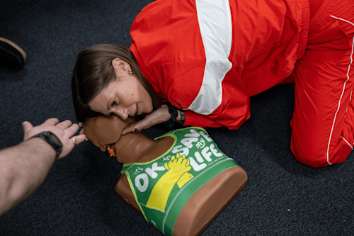A photograph of a woman in a red tracksuit practising first aid on a female Manikin, which is dressed in the CPR Bra.