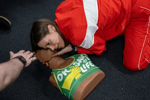 A photograph of a woman in a red tracksuit practising first aid on a female Manikin, which is dressed in the CPR Bra.