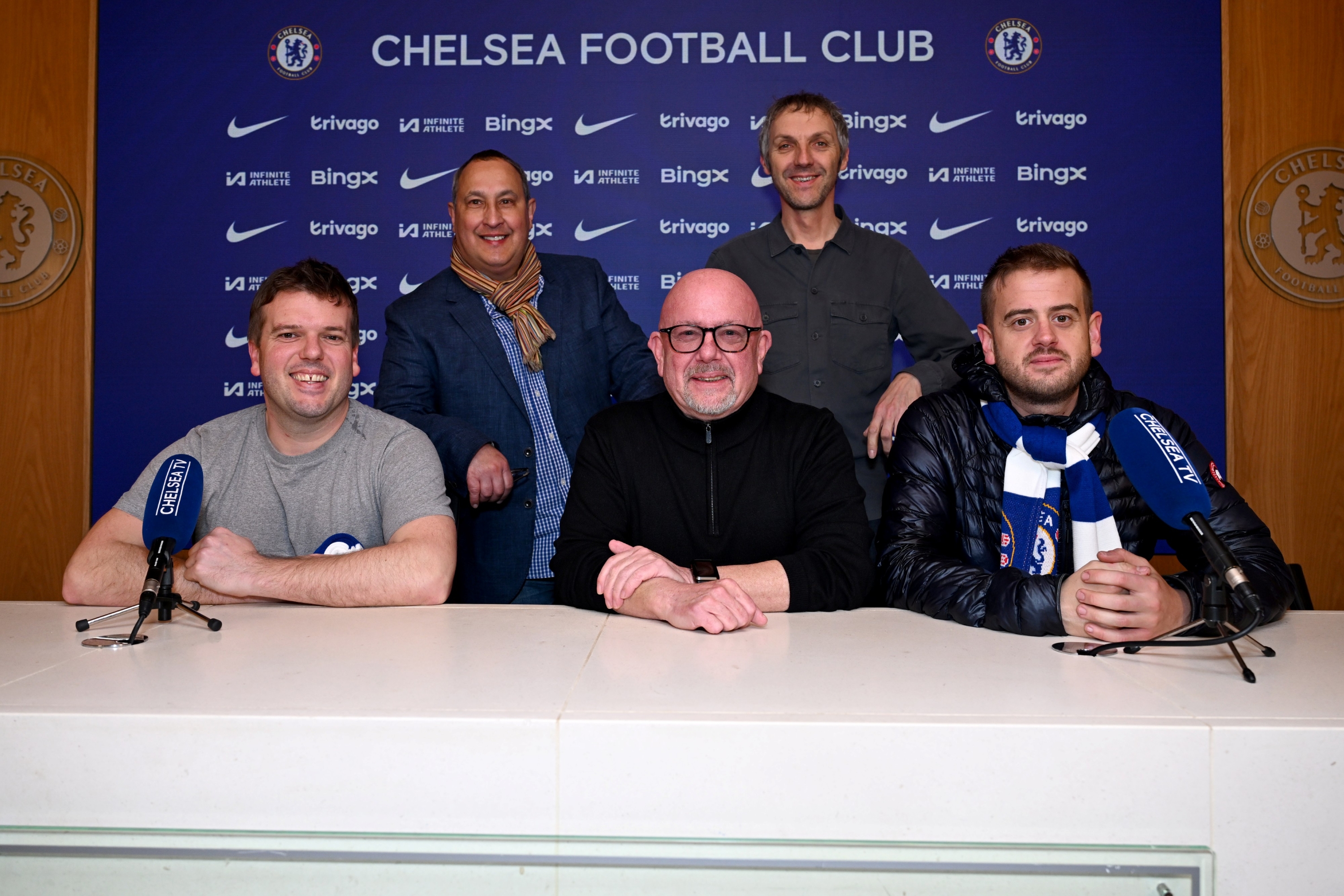 Paul Archer sat at a table with the Chelsea Football Club logo behind him surrounded by four of his friends and family.  