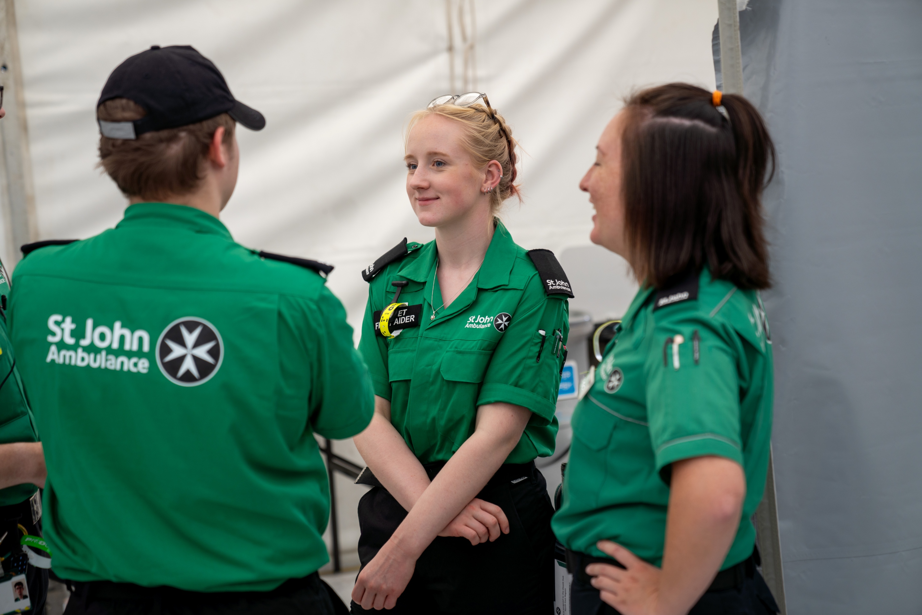 A Cadet First Aider standing in a tent in front of two adult volunteers. 