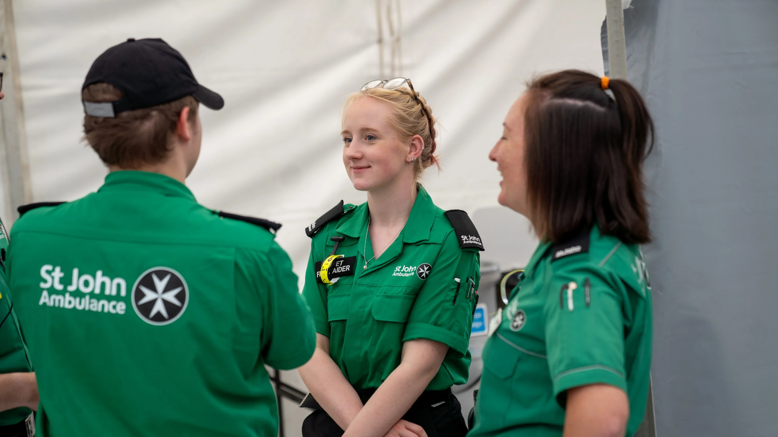 A Cadet First Aider standing in a tent in front of two adult volunteers.