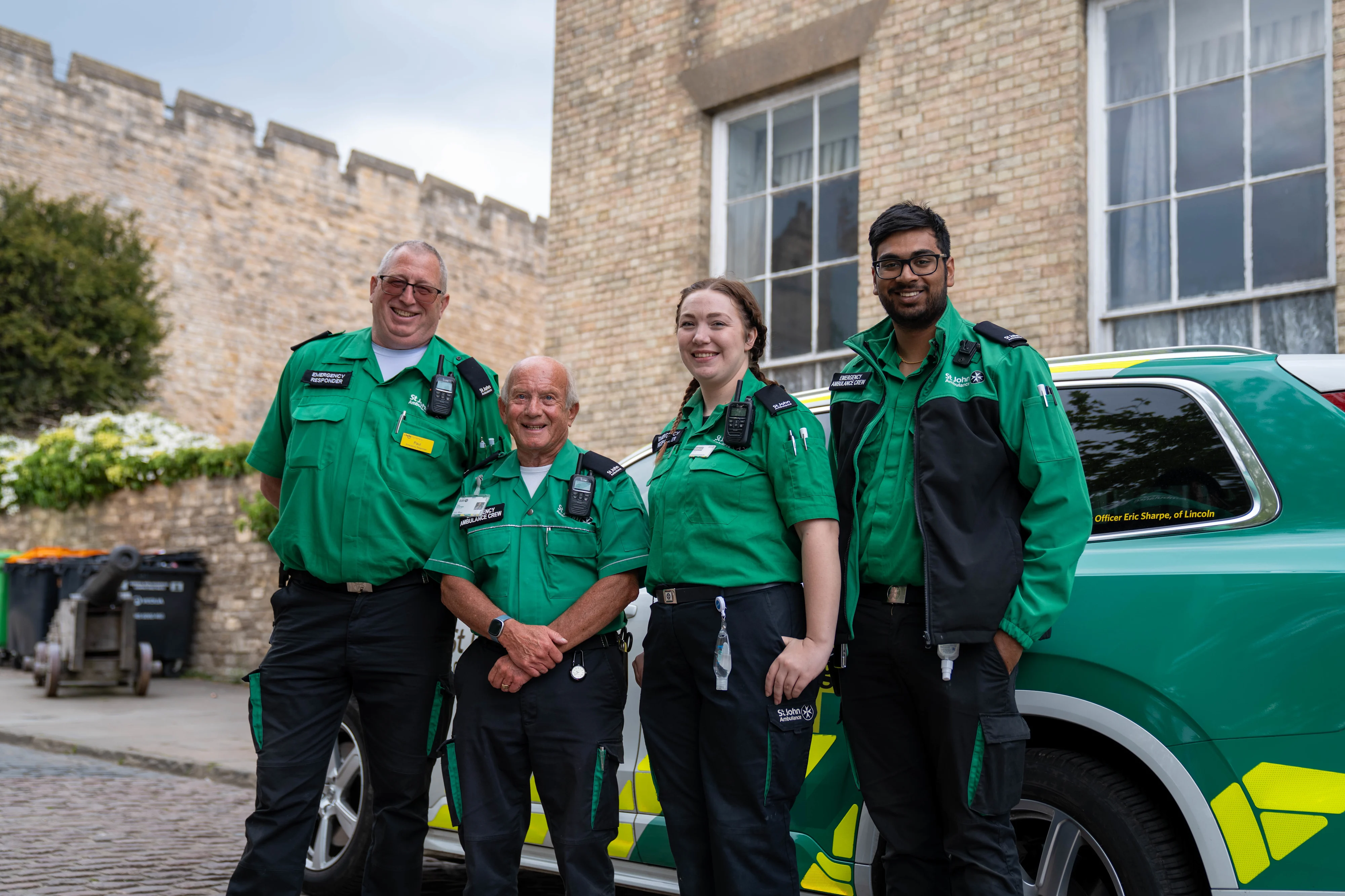 Four St John Ambulance volunteers stood smiling in front of an emergency responder vehicle.