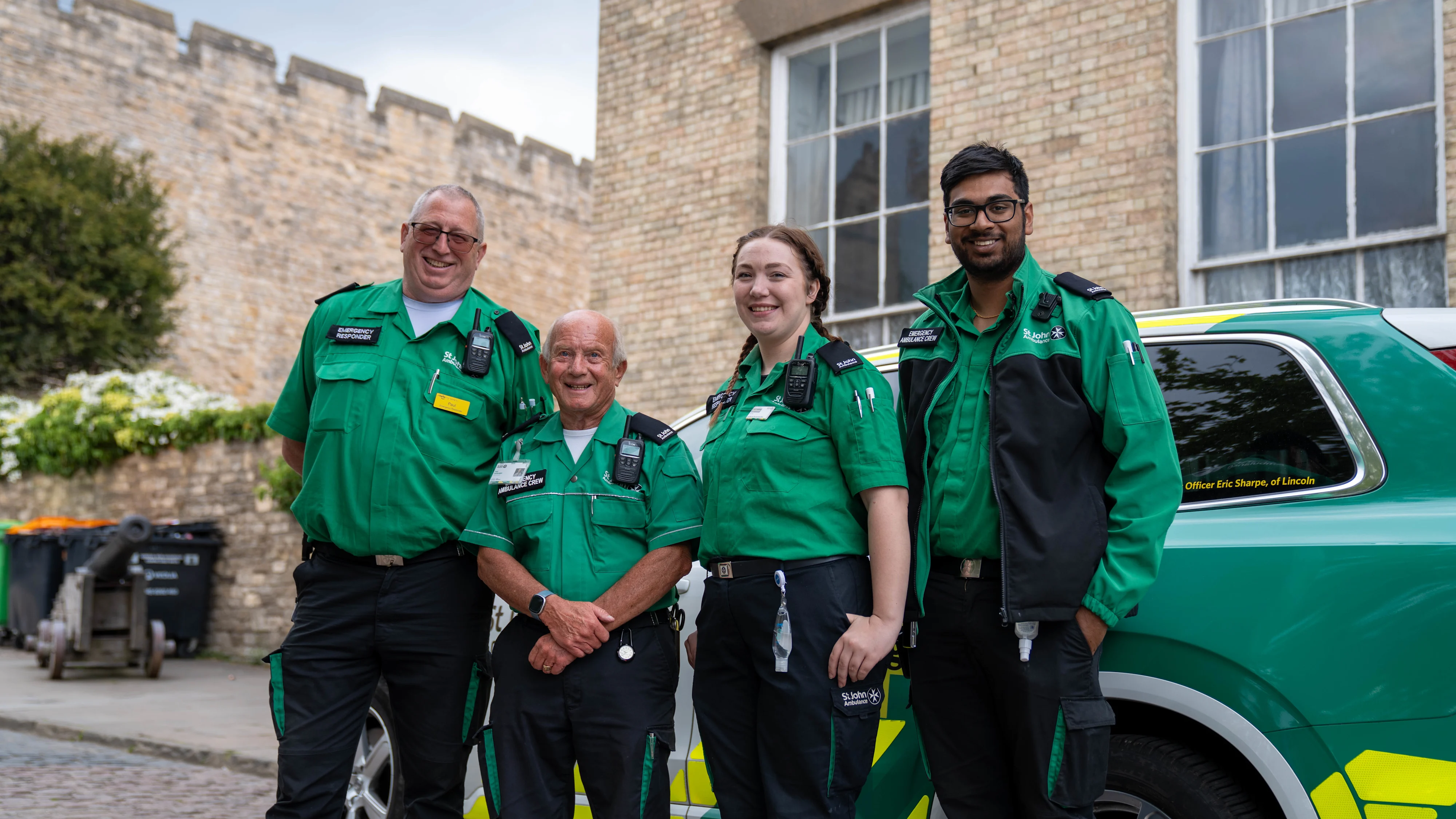 Four St John Ambulance volunteers stood smiling in front of an emergency responder vehicle.