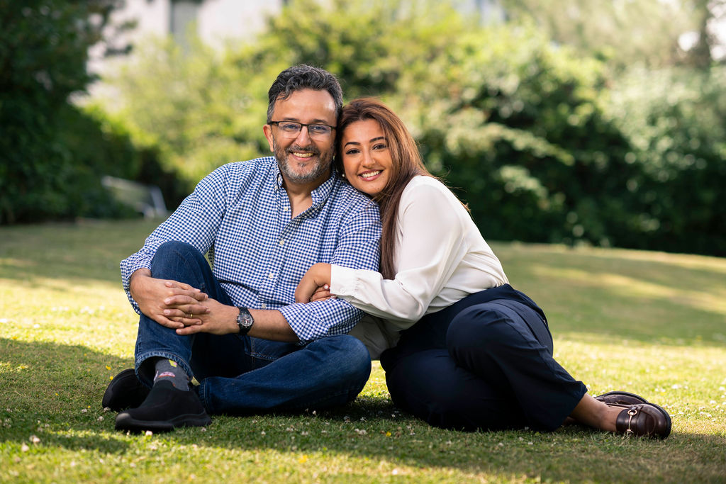 Hussam and Douaa sitting on grass, hugging and smiling at the camera.