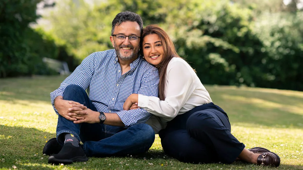 Hussam and Douaa sitting on grass, hugging and smiling at the camera.
