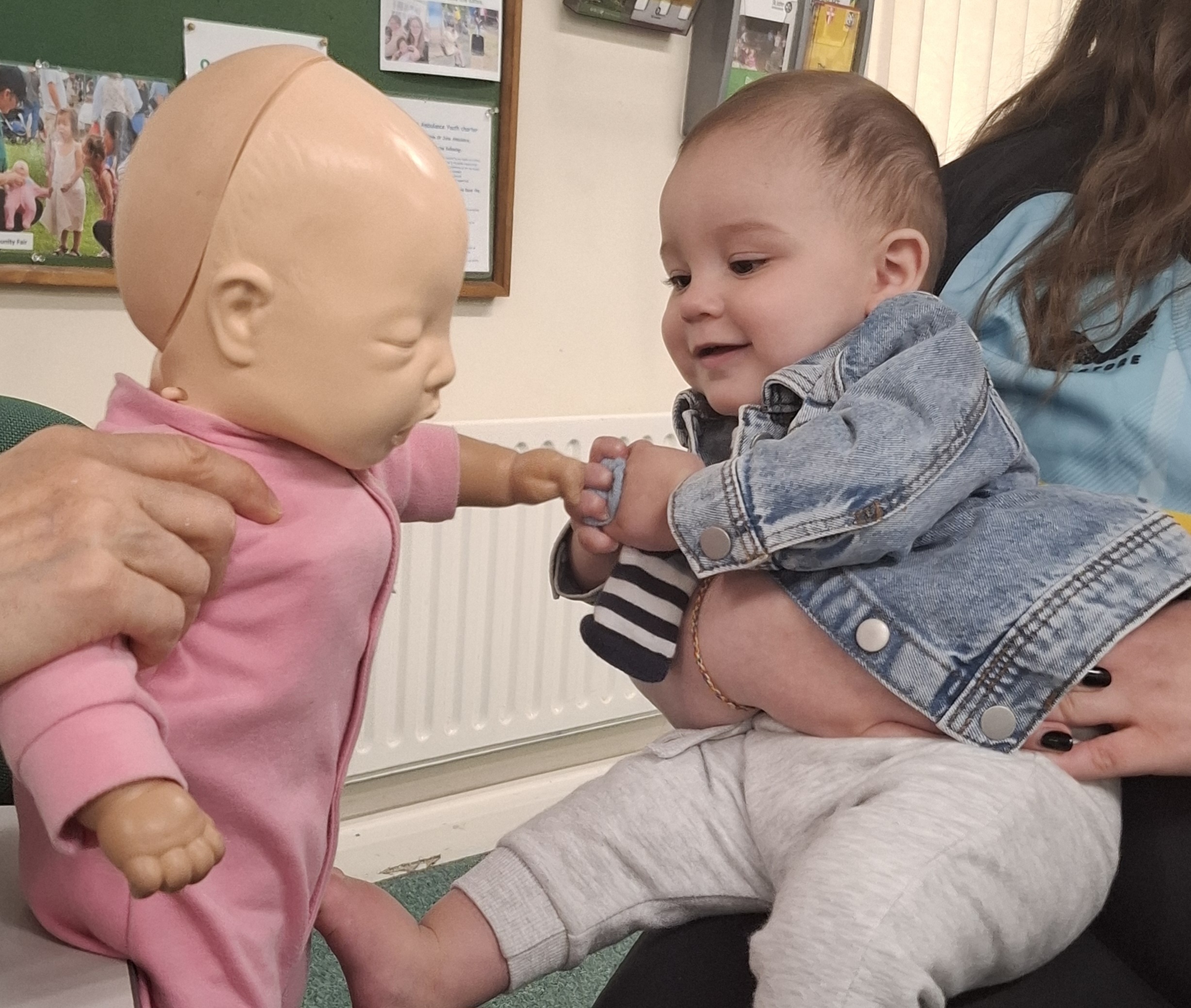 A photograph of Leah's baby, Cayden, smiling and reaching out to a baby Manikin.