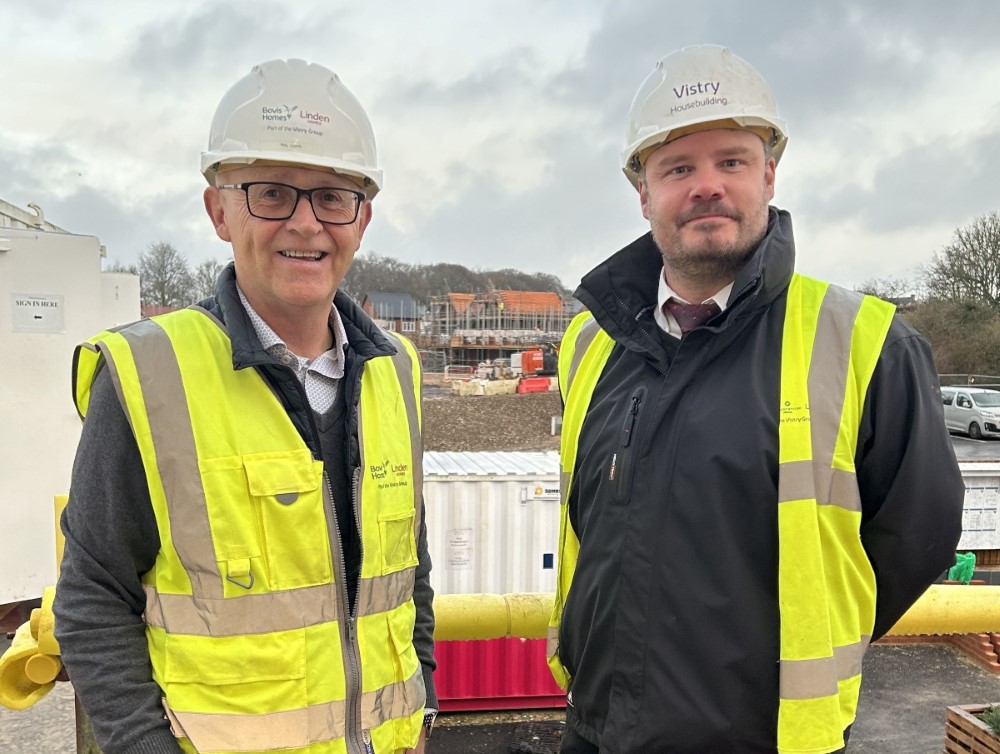 A photograph of Phil Lloyd (left) and James Berry (right) standing together on a construction site. Both men are wearing hi-vis vests and hard hats, and are smiling at the camera.