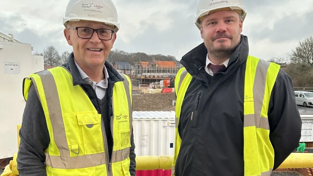 A photograph of Phil Lloyd (left) and James Berry (right) standing together on a construction site. Both men are wearing hi-vis vests and hard hats, and are smiling at the camera.