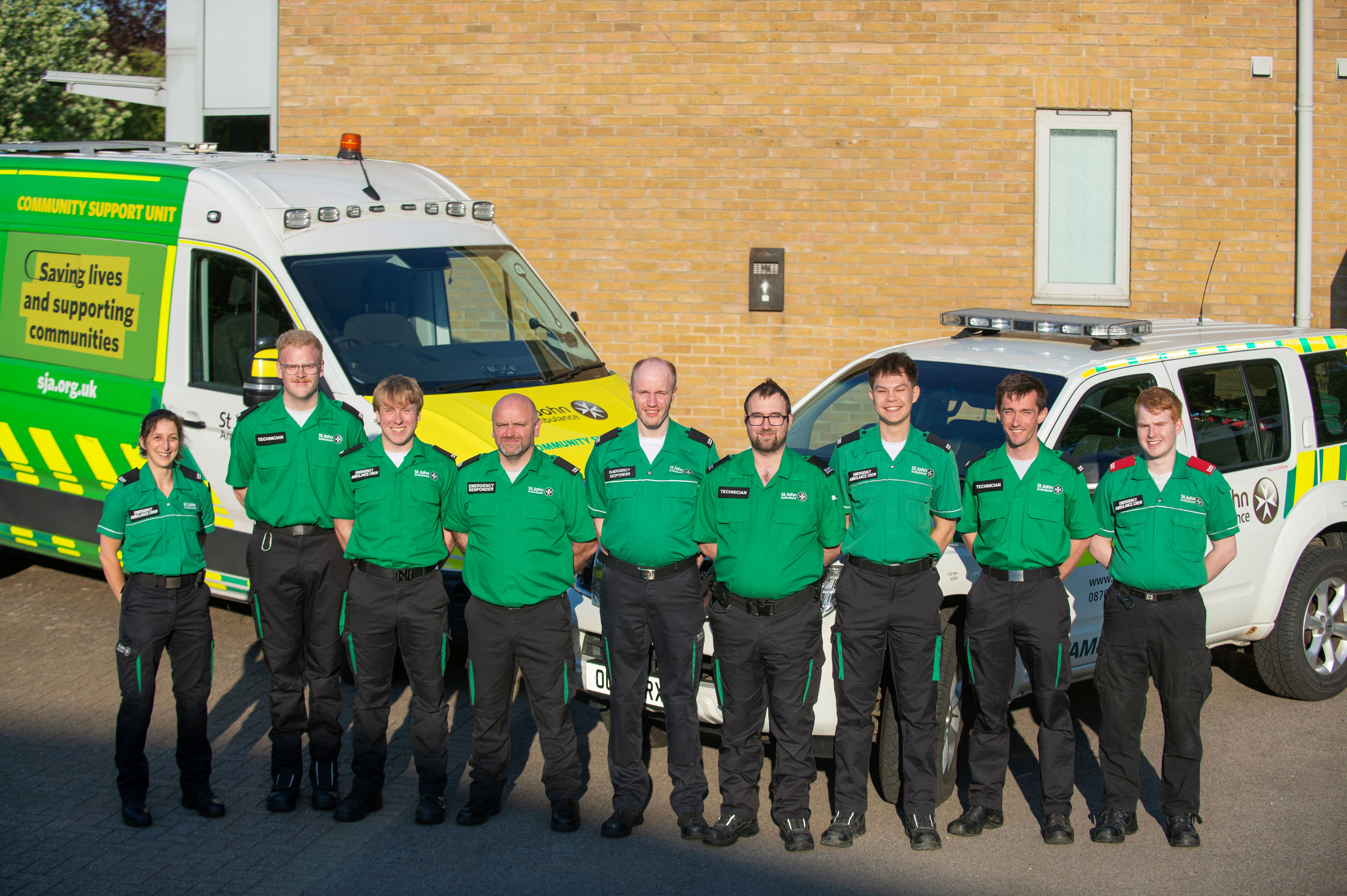 St John Ambulance Co-Responder team stood outside in front of an ambulance and a responder vehicle.