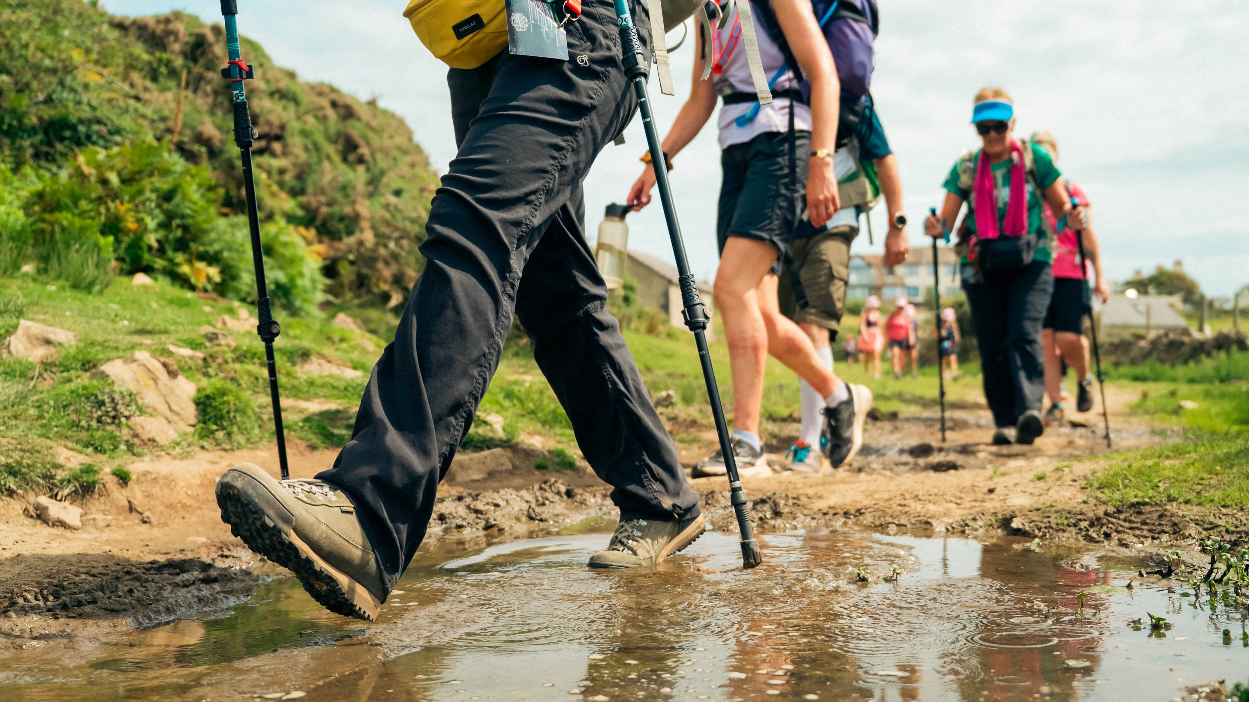 A group of people in hiking gear and using walking sticks walking along a very muddy and wet footpath.