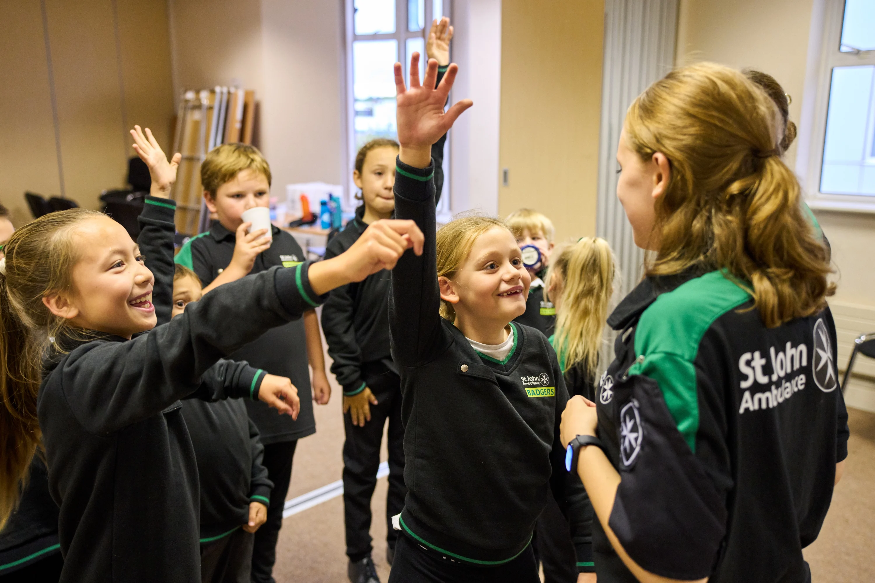 A group of Badgers inside standing in front of a Youth Leader smiling. Some of the Badgers have their hands up.