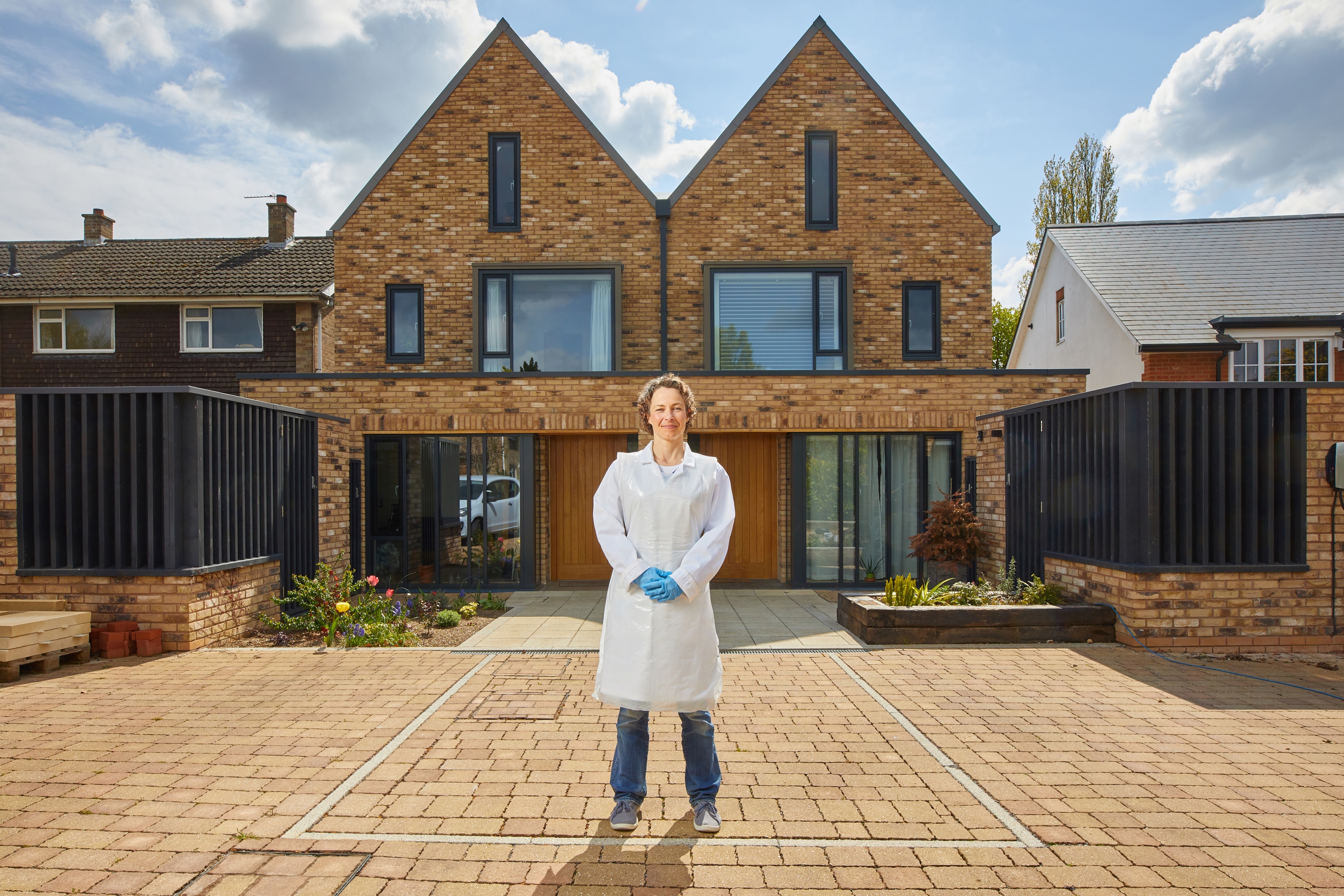 A photograph of Claire standing in front of a house, wearing a lab coat and gloves.