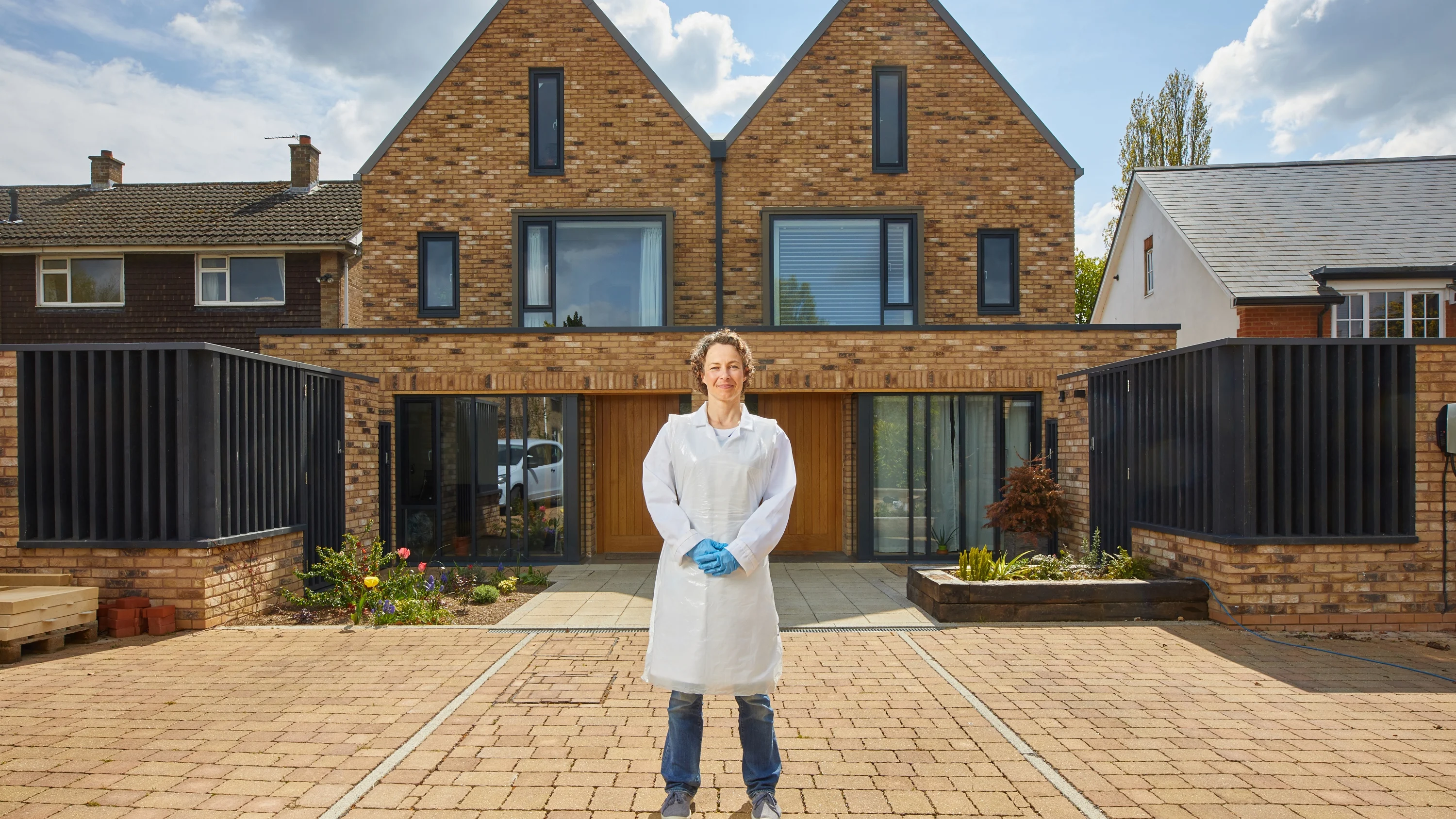 A photograph of Claire standing in front of a house, wearing a lab coat and gloves.