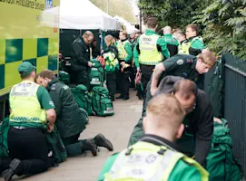 A photograph of SJA volunteers working with NHS paramedics. Ambulances and medical tents can be seen in the background.