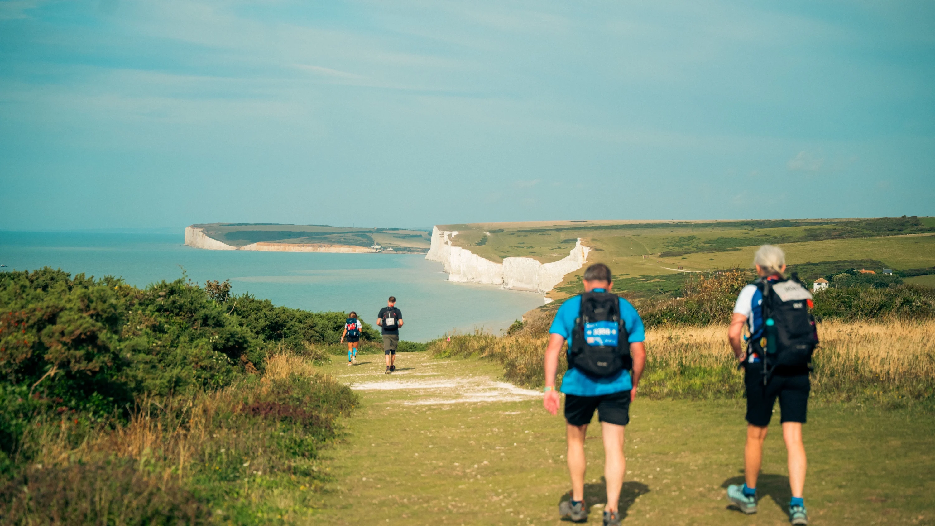 Four people walking along the South Downs coastal path. In the distance are white cliffs and the sea.