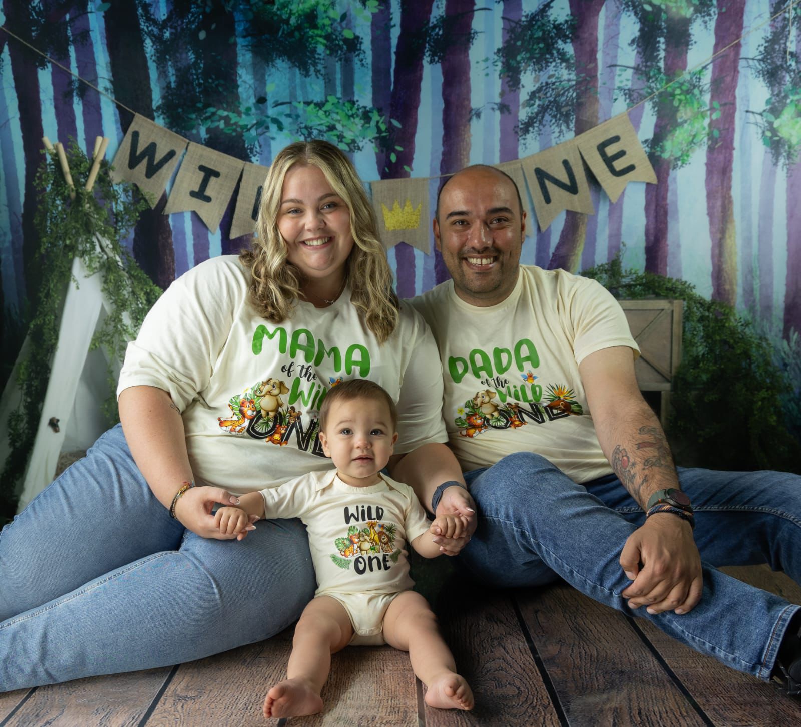 A photograph of Leah Weenen, her baby, Cayden, and husband Charlie Abel, smiling to camera and wearing matching 'Mama' and 'Dada' t-shirts. 