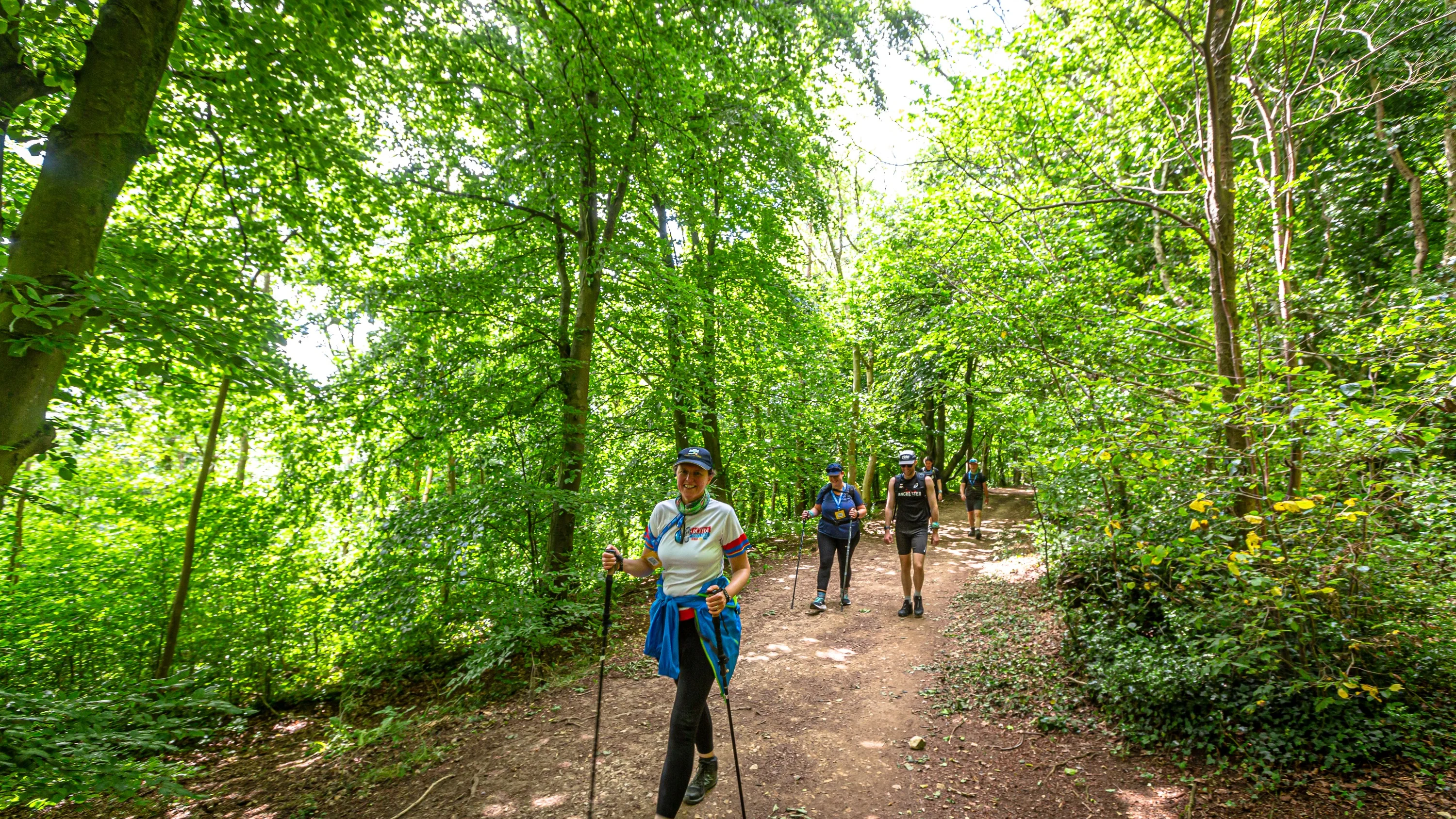 Three people with walking sticks walking along a footpath through some woods.