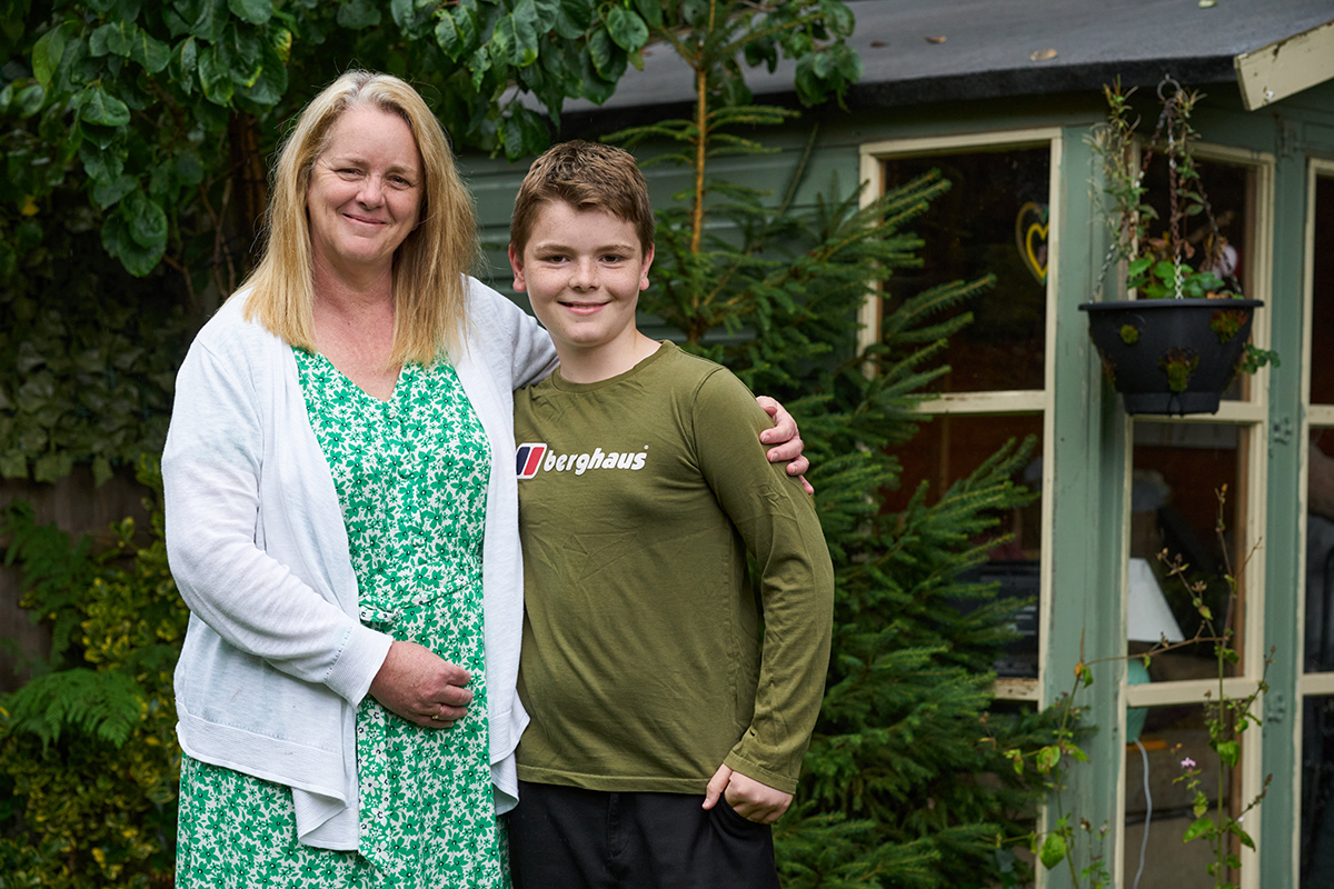 A photograph of Anne-Marie and her son, George, smiling and hugging in their garden.