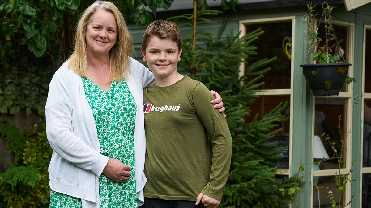 A photograph of Anne-Marie and her son, George, smiling and hugging in their garden.