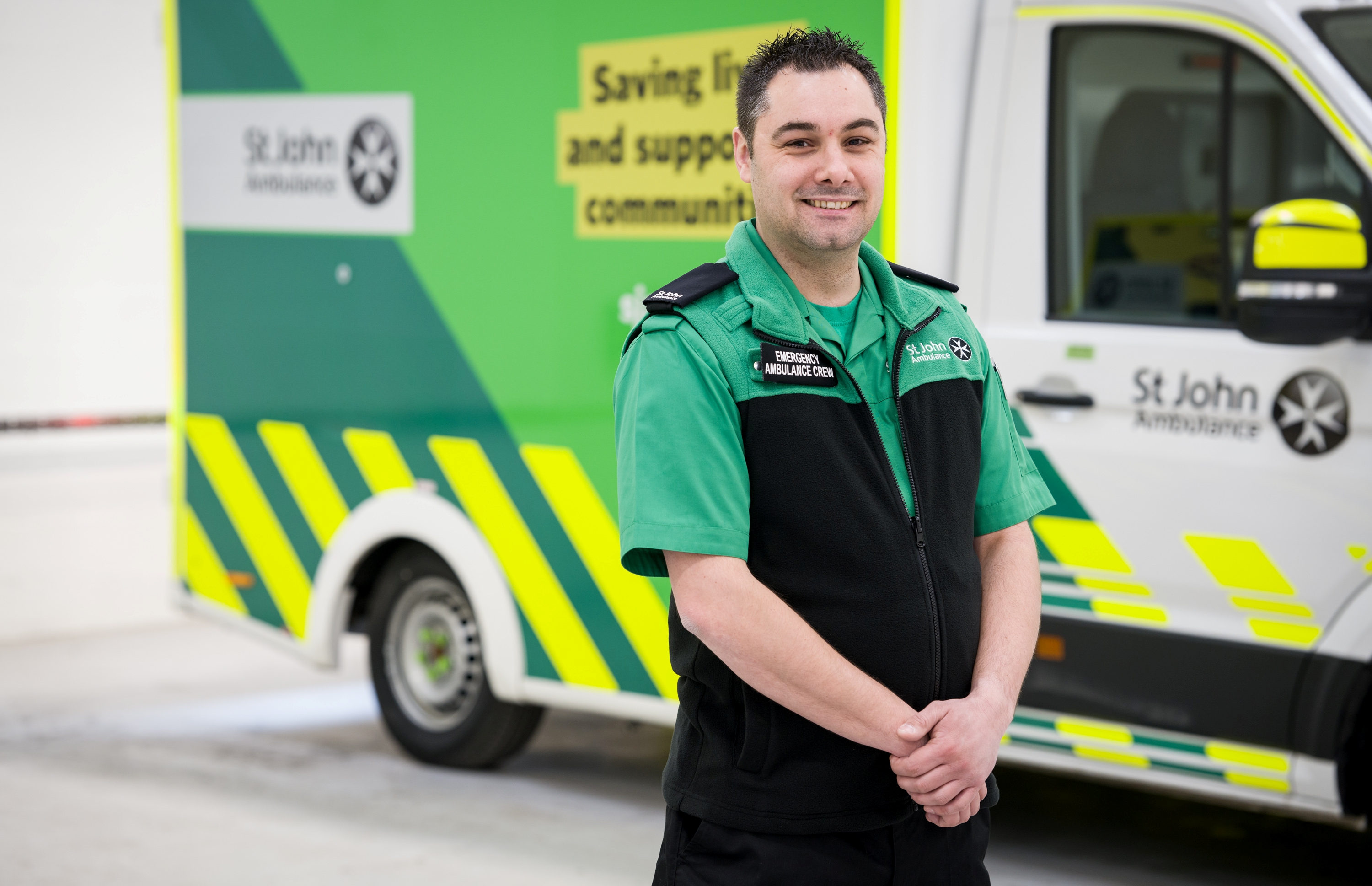 A member of the St John Ambulance emergency crew posing in front of an ambulance with a smile.