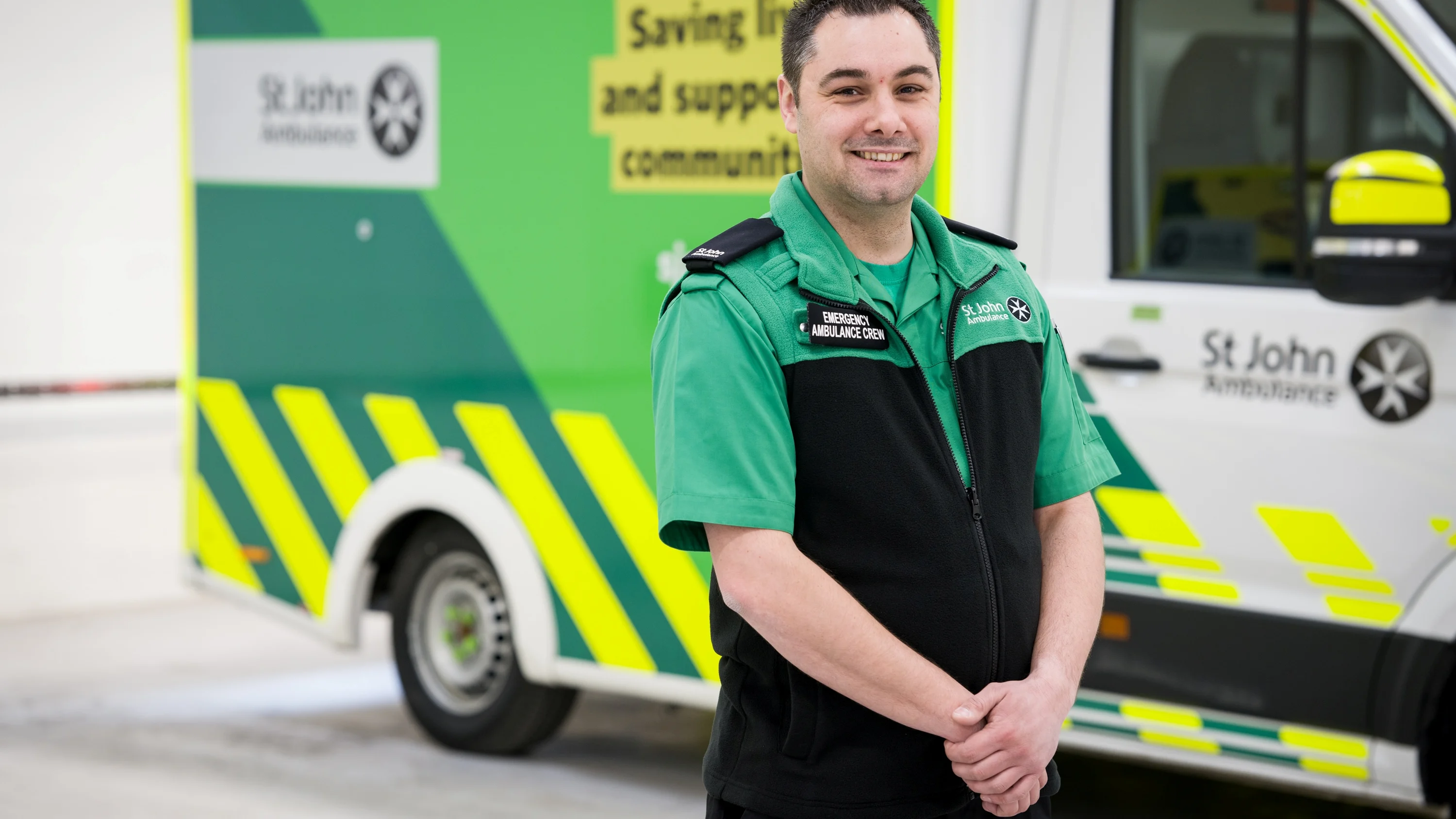 A member of the St John Ambulance emergency crew posing in front of an ambulance with a smile.