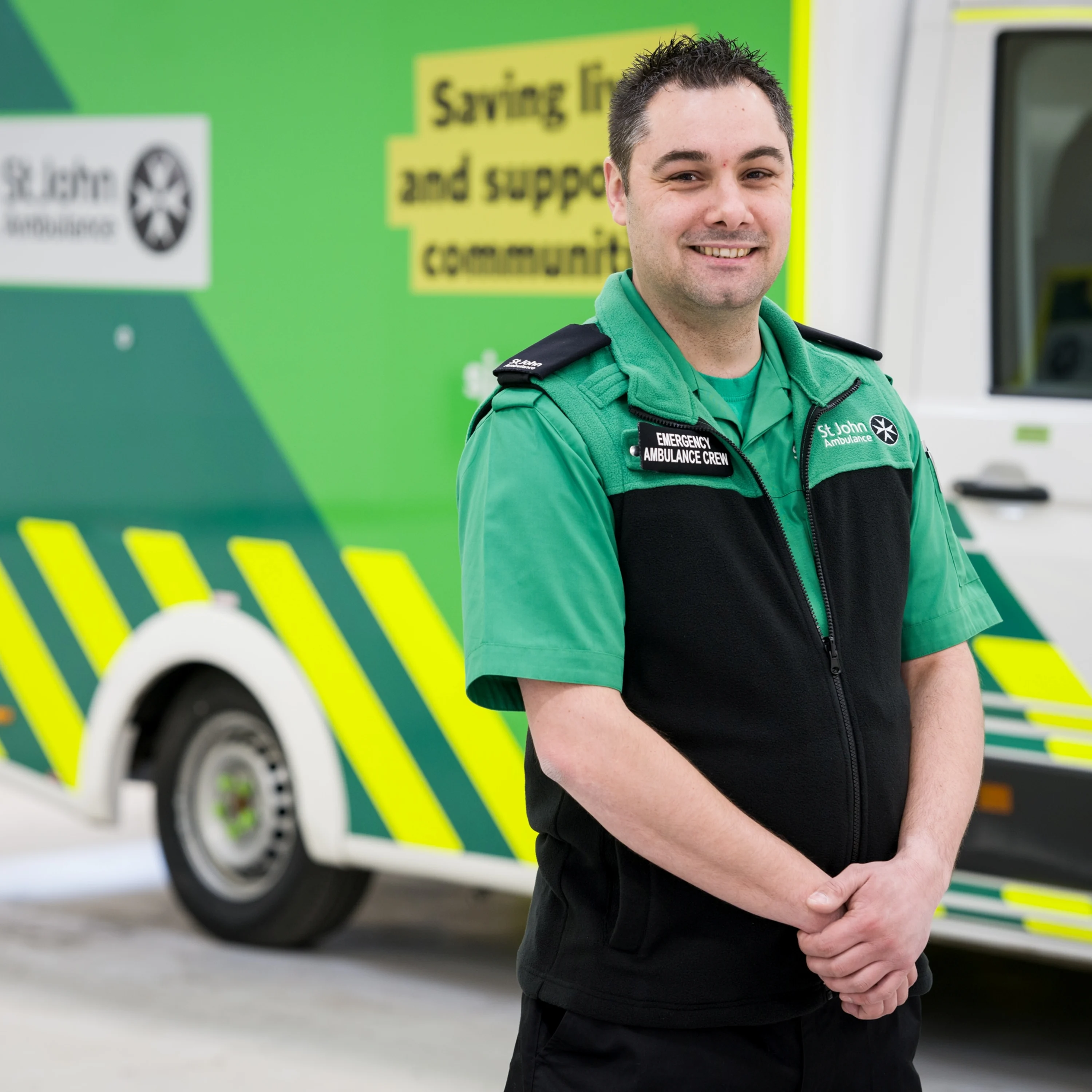 A member of the St John Ambulance emergency crew posing in front of an ambulance with a smile.