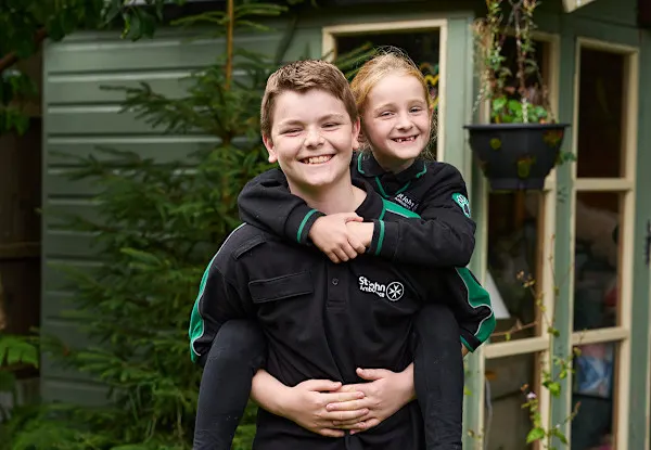 A photograph of George and his sister Mary in their garden. Both of them are wearing their St John uniform. George is carrying Mary on his back and they are both smiling.