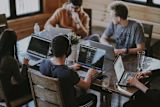 Decorative image of a group of five people working on their laptops around a table