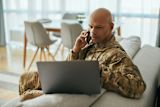 Person in military uniform on a phone call and using a laptop