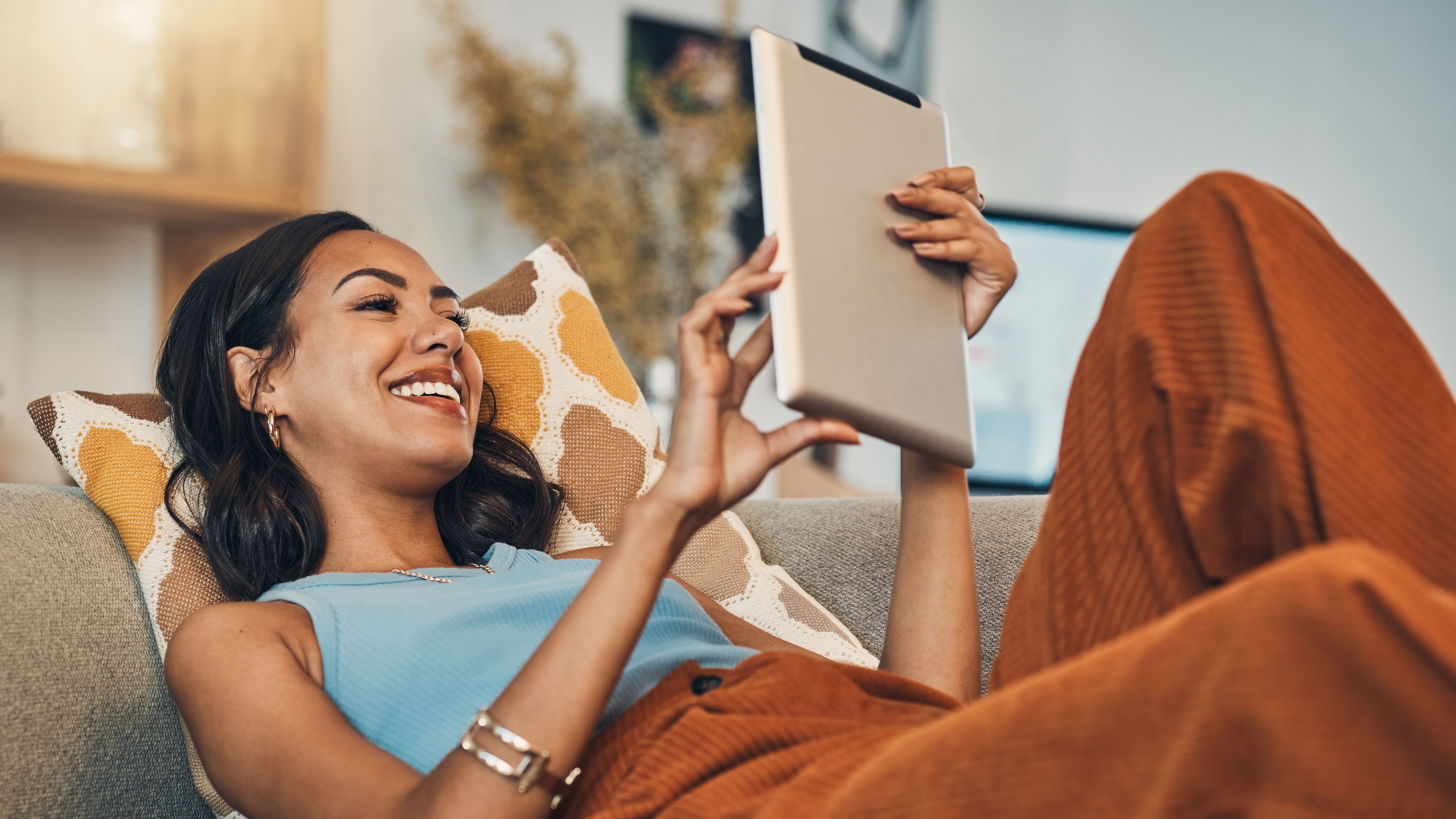 Eine junge Frau liegt mit dem Tablet auf der Couch und erkundigt sich nach günstigem Strom der NEW Energie.