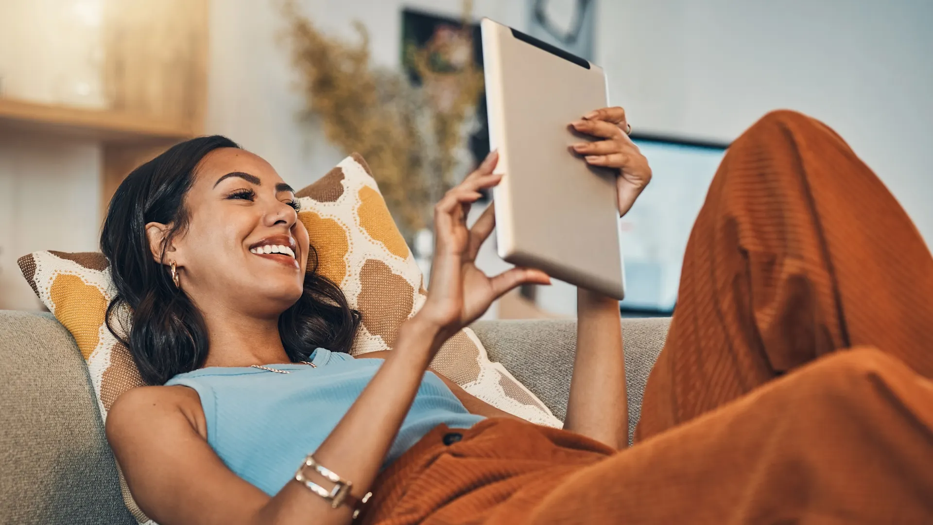 Auswahl von günstigem Strom Eine junge Frau liegt mit dem Tablet auf der Couch und erkundigt sich nach günstigem Strom der NEW Energie.