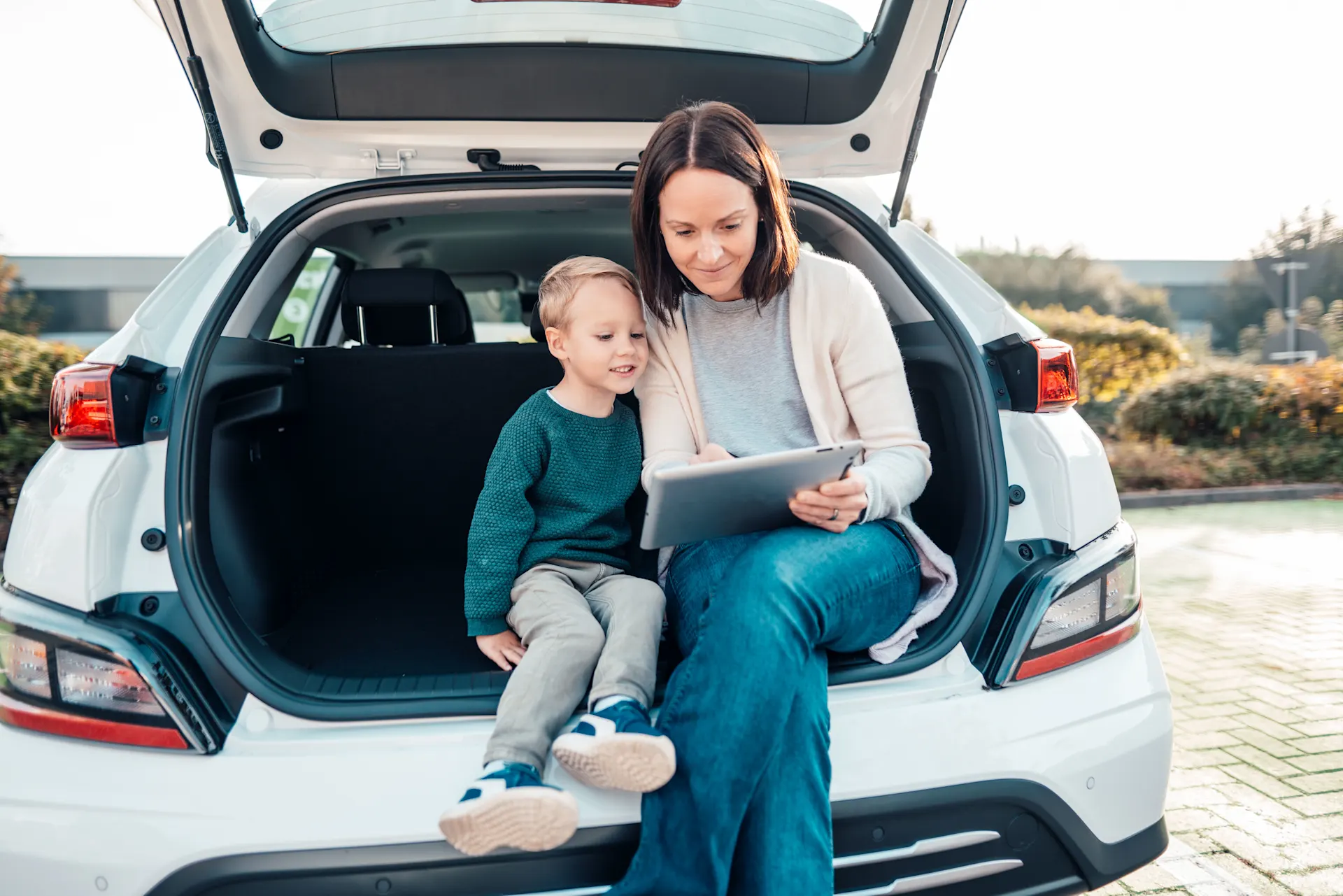 Eine Mutter sitzt mit ihrem Sohn in einem E-Auto. Sie beobachten auf einem Tablet den Ladevorgang.