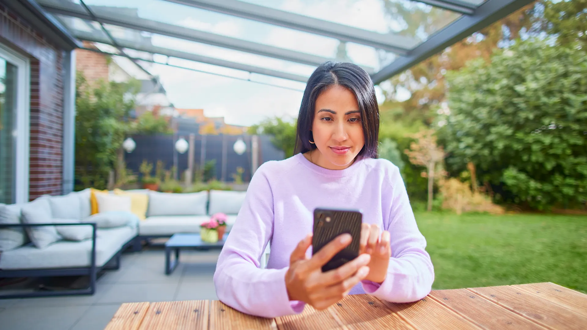 NEW Dienstleistungen Eine Frau sitzt im Garten mit ihrem Smartphone und informiert sich über die Dienstleistungen und den Service bei der NEW Energie.