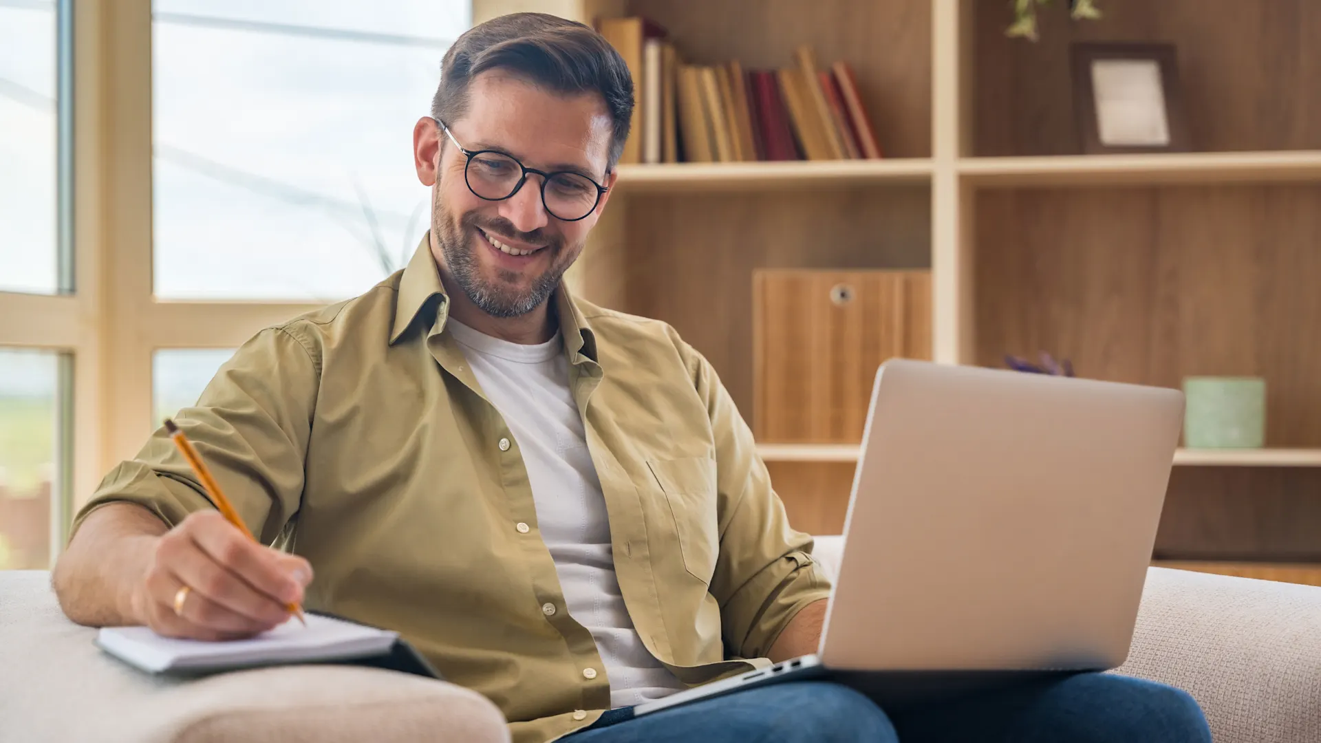 E-Rechnung bei der NEW Energie Ein Mann sitzt mit einem Laptop auf dem Schoß auf dem Sofa und informiert sich über E-Rechnungen bei der NEW Energie.