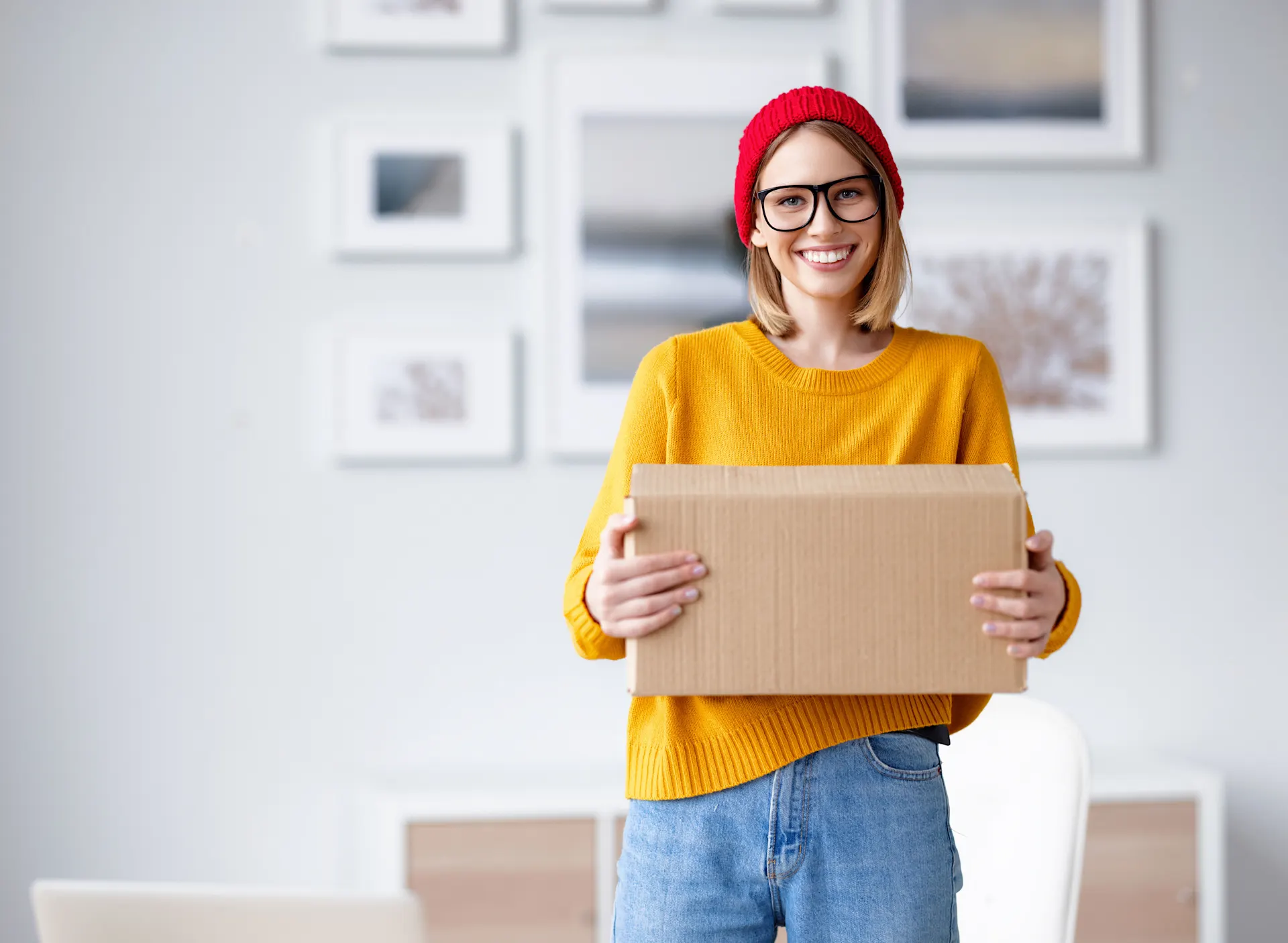 Eine Frau mit roter Mütze steht in ihrem Wohnzimmer und hält ein Paket von der NEW Energie in der Hand.