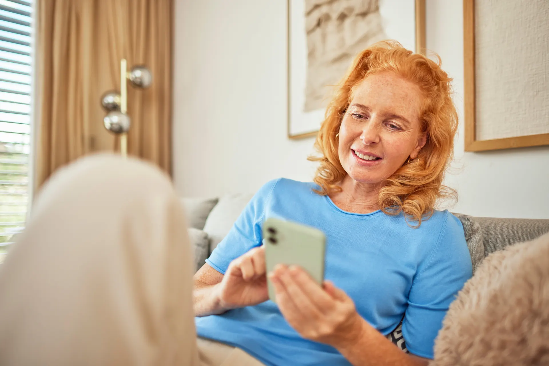 Online seine Angelegenheiten regeln Eine Frau sitzt mit ihrem Smartphone auf dem Sofa und informiert sich über günstige Tarife, Services und Wissenswertes der NEW Energie.