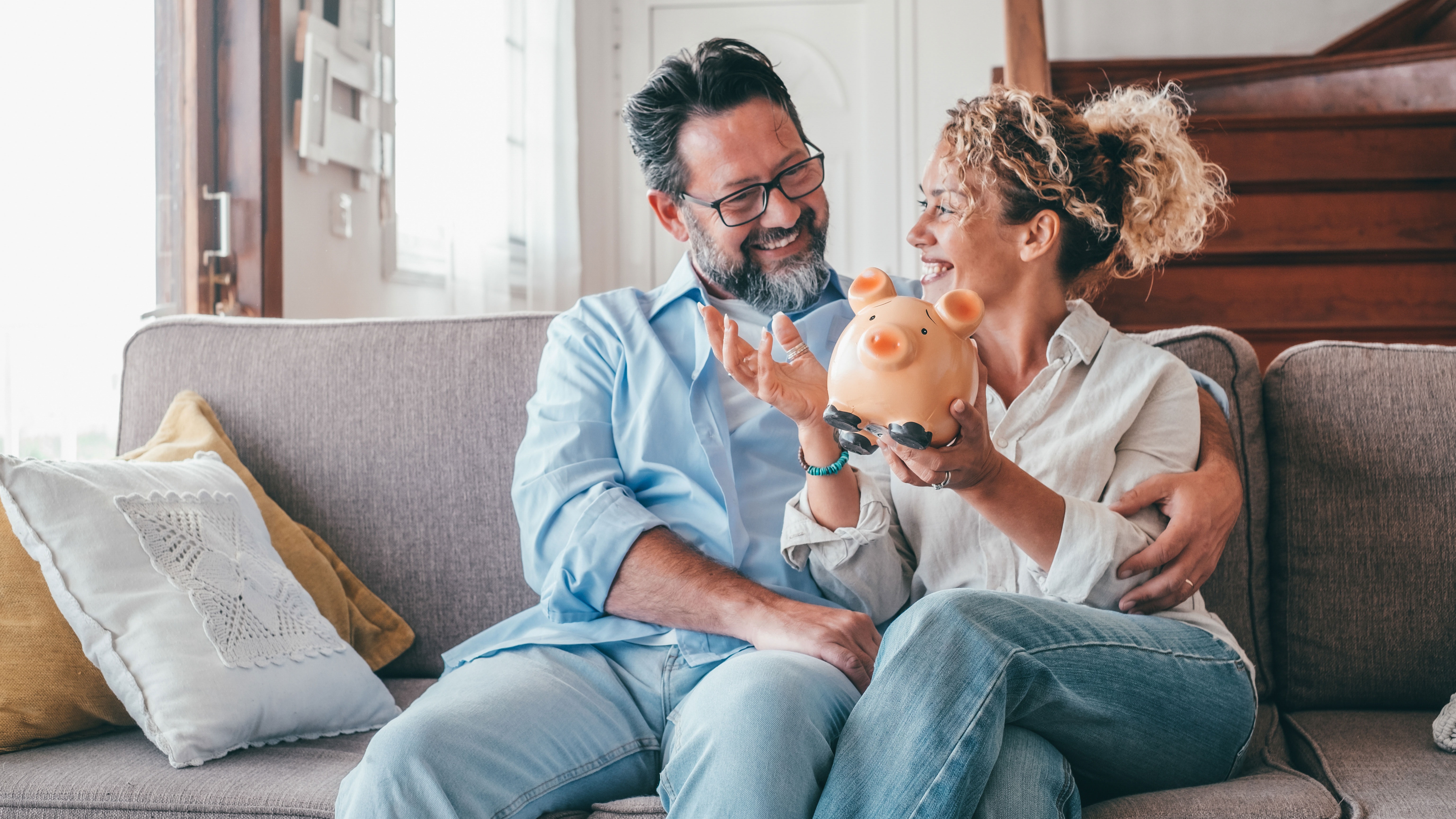 Frau und Mann sitzen auf einer Couch und halten ein Sparschwein in der Hand.