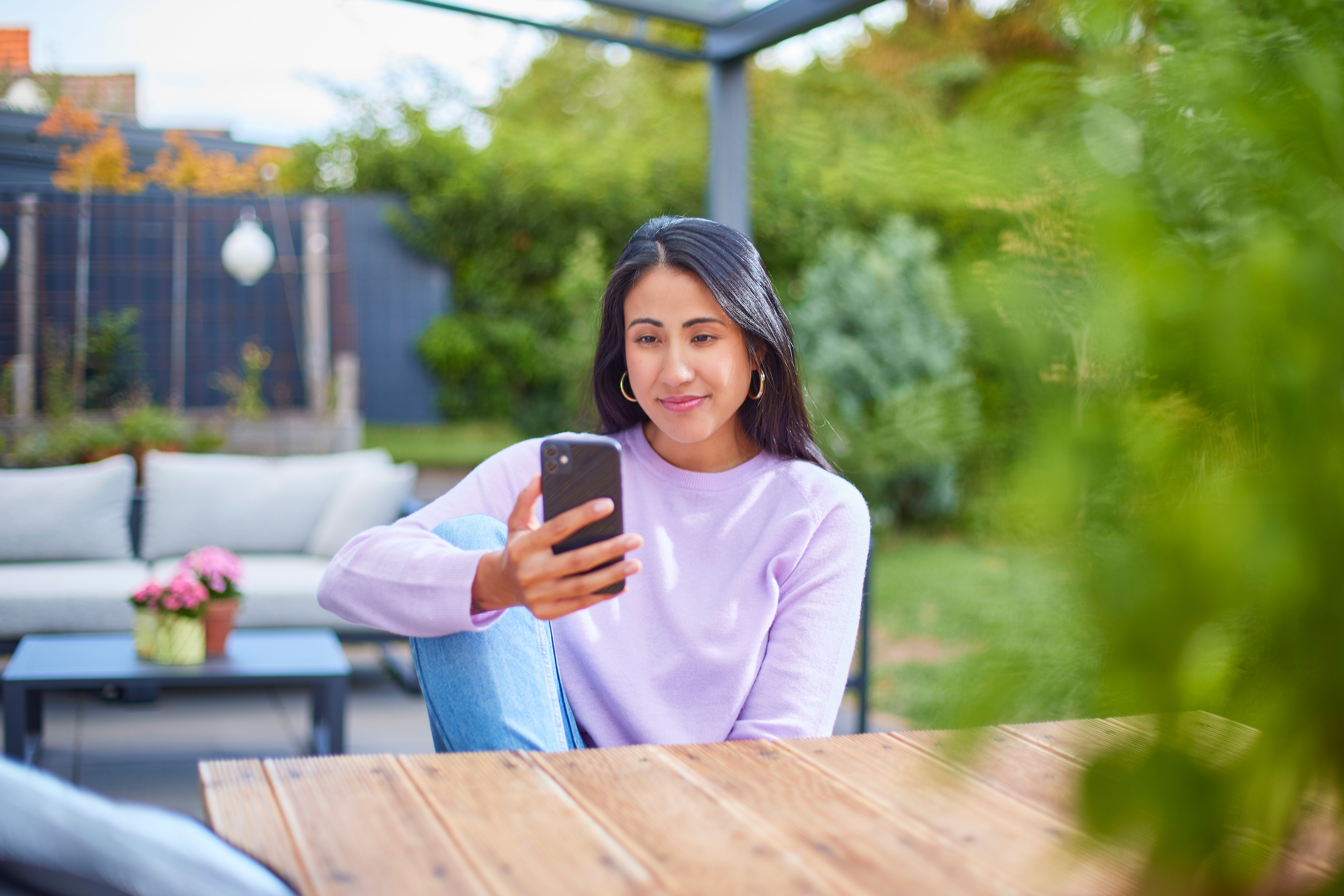Eine Frau sitzt im Garten mit einem Smartphone und informiert sich über günstige Tarife und günstige Energie der NEW Energie.