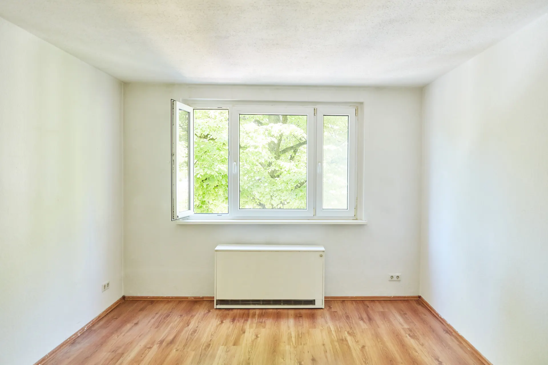 Nachtspeicherheizung im Zimmer Eine Nachtspeicherheizung der NEW Energie steht in einem Zimmer unter einem Fenster.