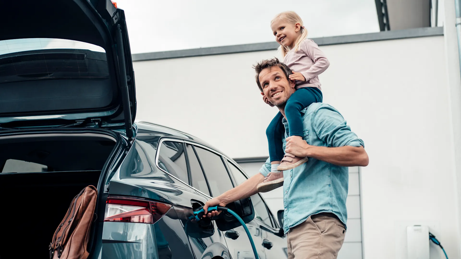 Auto mit Ökostrom laden Ein Kind sitzt beim Vater auf den Schultern während der Vater das E-Auto mit Ökostrom der NEW Energie lädt.