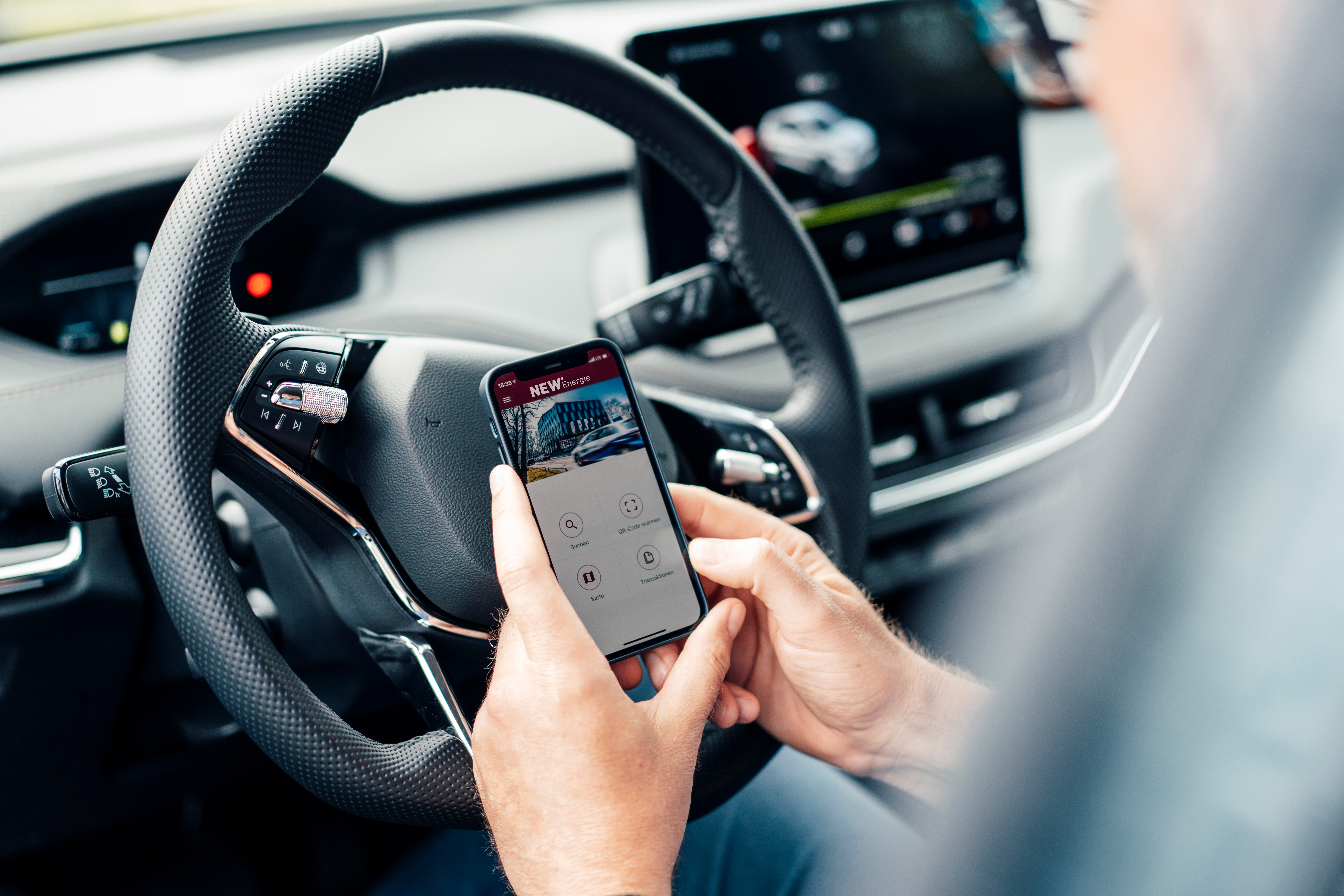 Ein Mann sitzt in seinem Auto und hält ein Smartphone in der Hand und schaut sich eine App der NEW Energie an.
