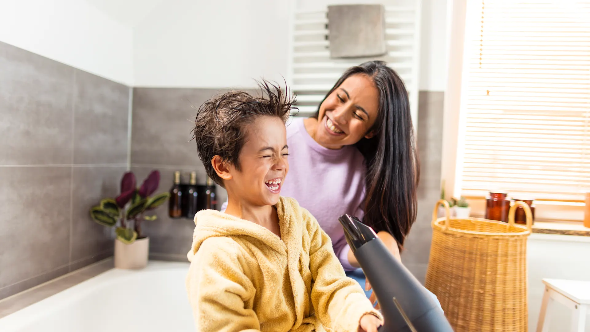 Haare föhnen mit der NEW Energie Ein kleiner Junge föhnt sich im Beisein seiner Mutter die Haare im Badezimmer. Strom bekommt der Föhn durch die NEW Energie.