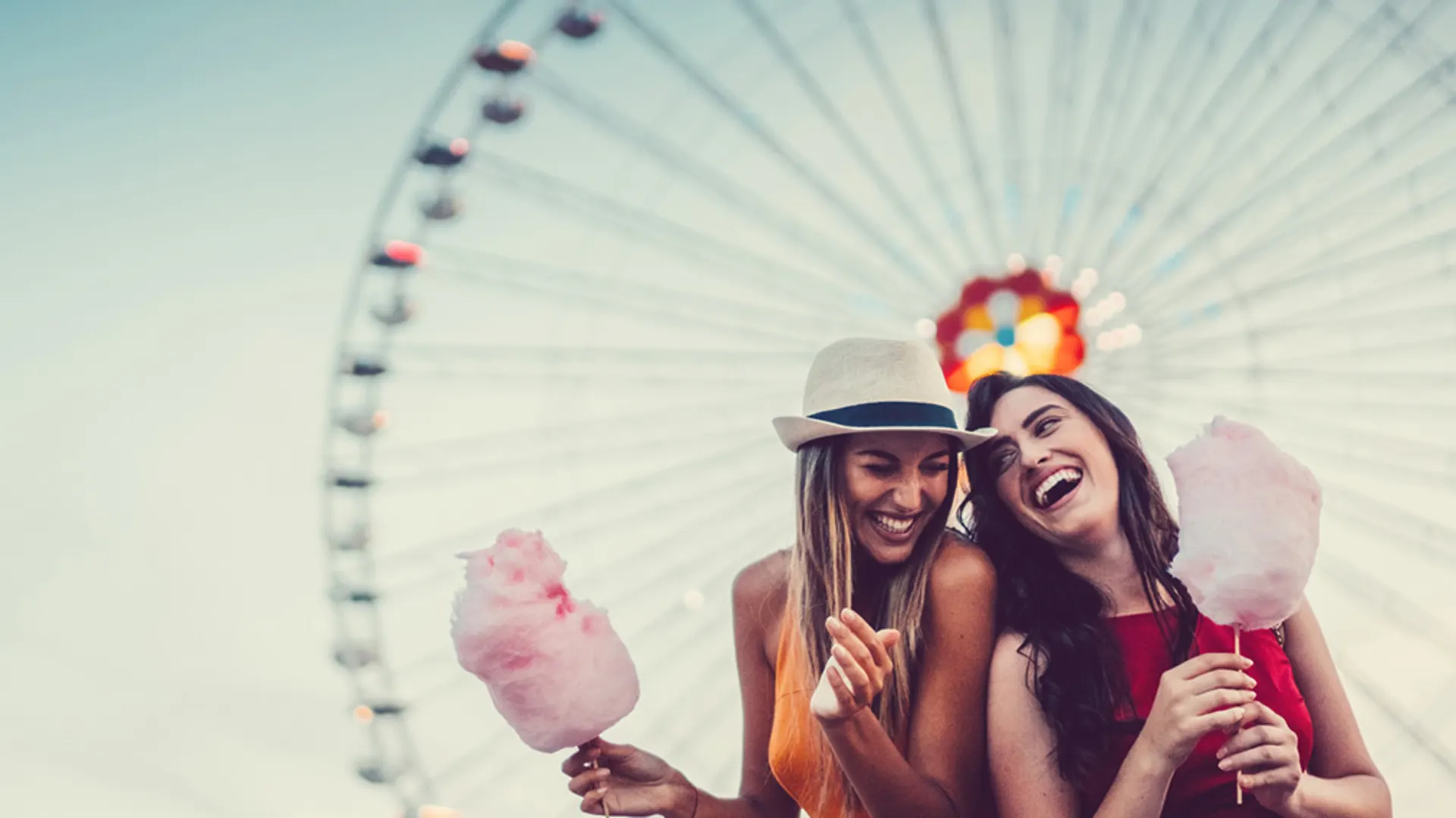 Freundinnen vor Riesenrad Zwei Freundinnen stehen vor einem Riesenrad und essen Zuckerwatte gemeinsam. Sie freuen sich über die Vorteile bei der NEW Energie.