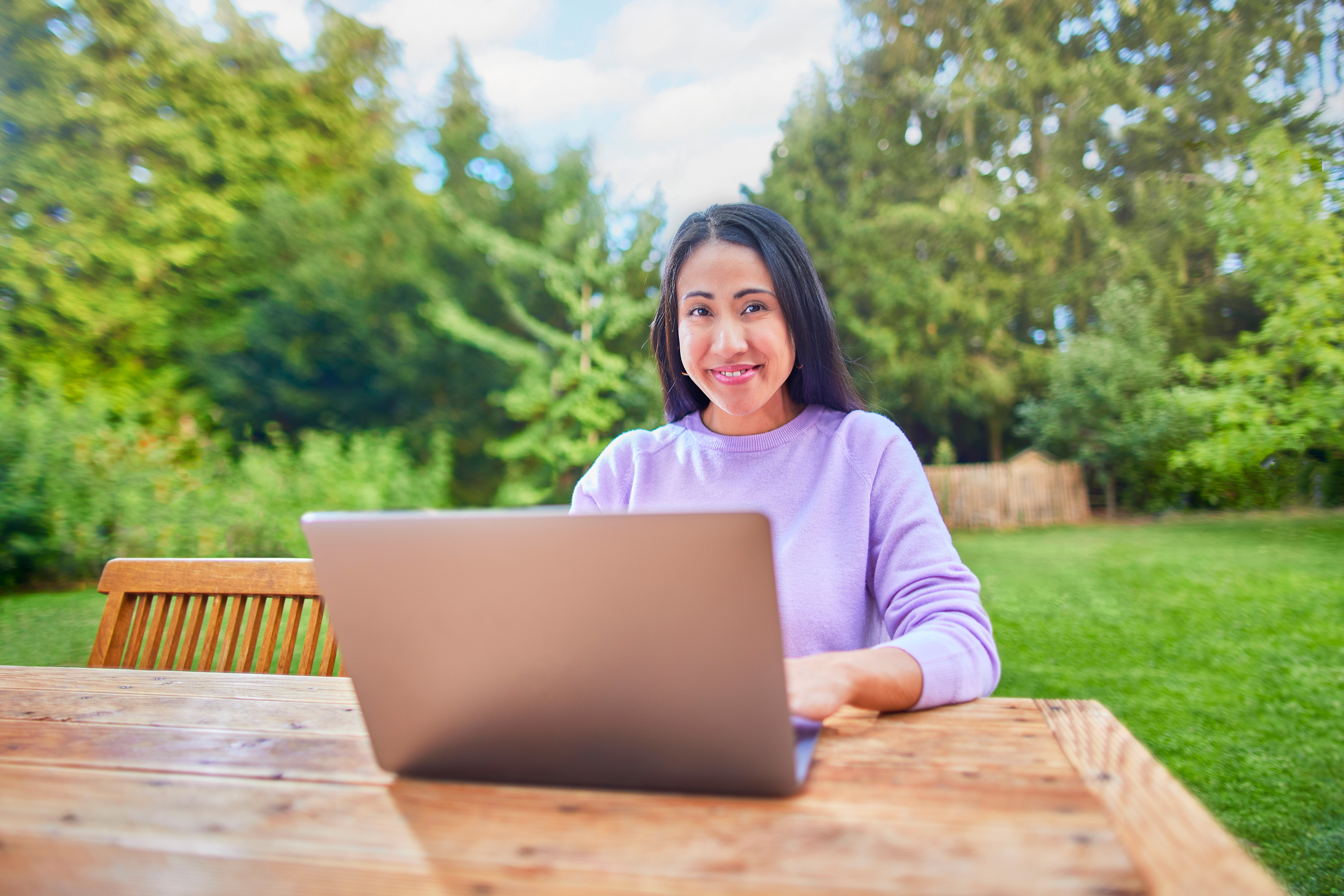 Eine Frau sitzt mit ihrem Laptop im Garten und informiert sich über die Tarifauswahl der NEW Energie.