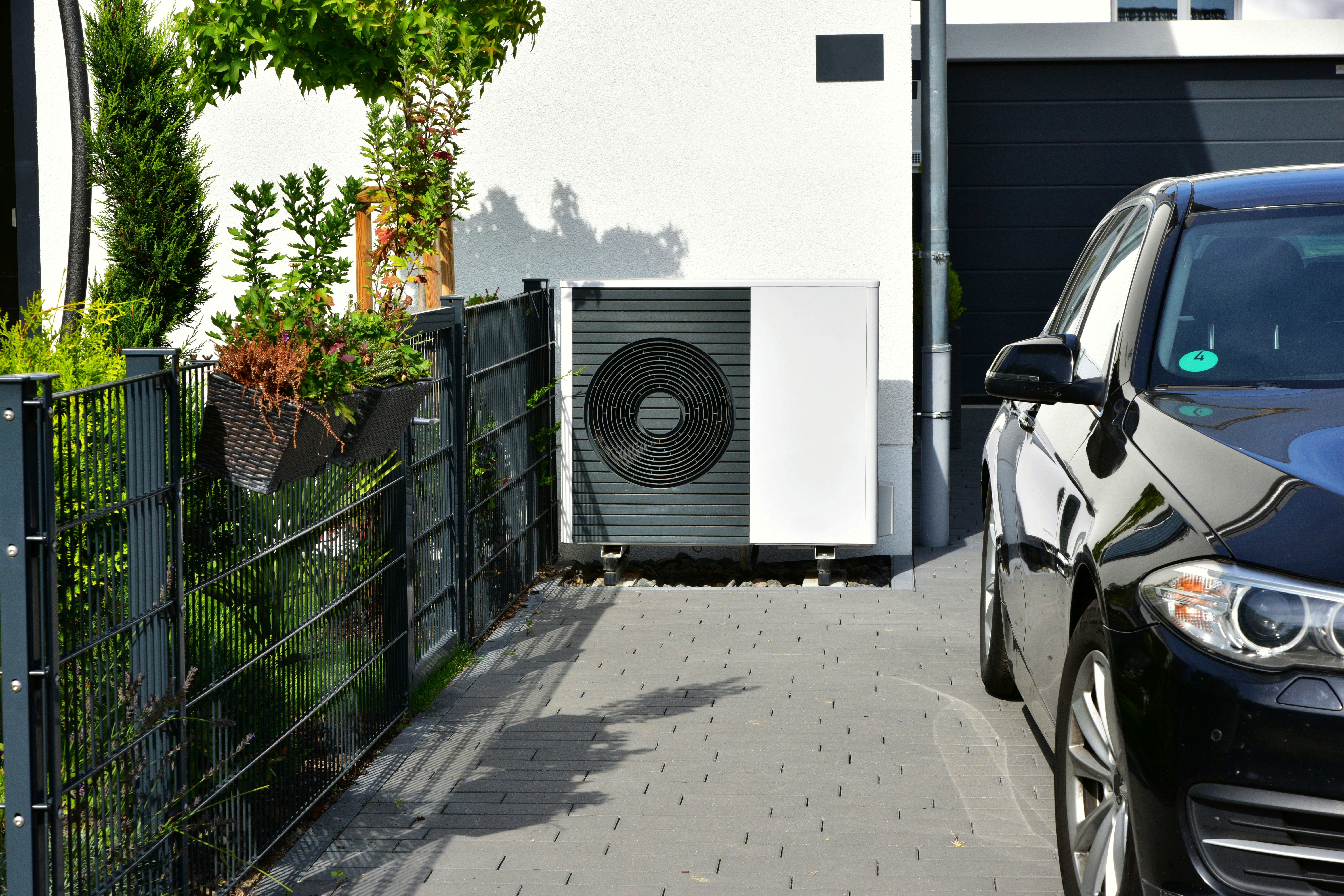 Eine Wärmepumpe steht an einer Garage im Außenbereich.