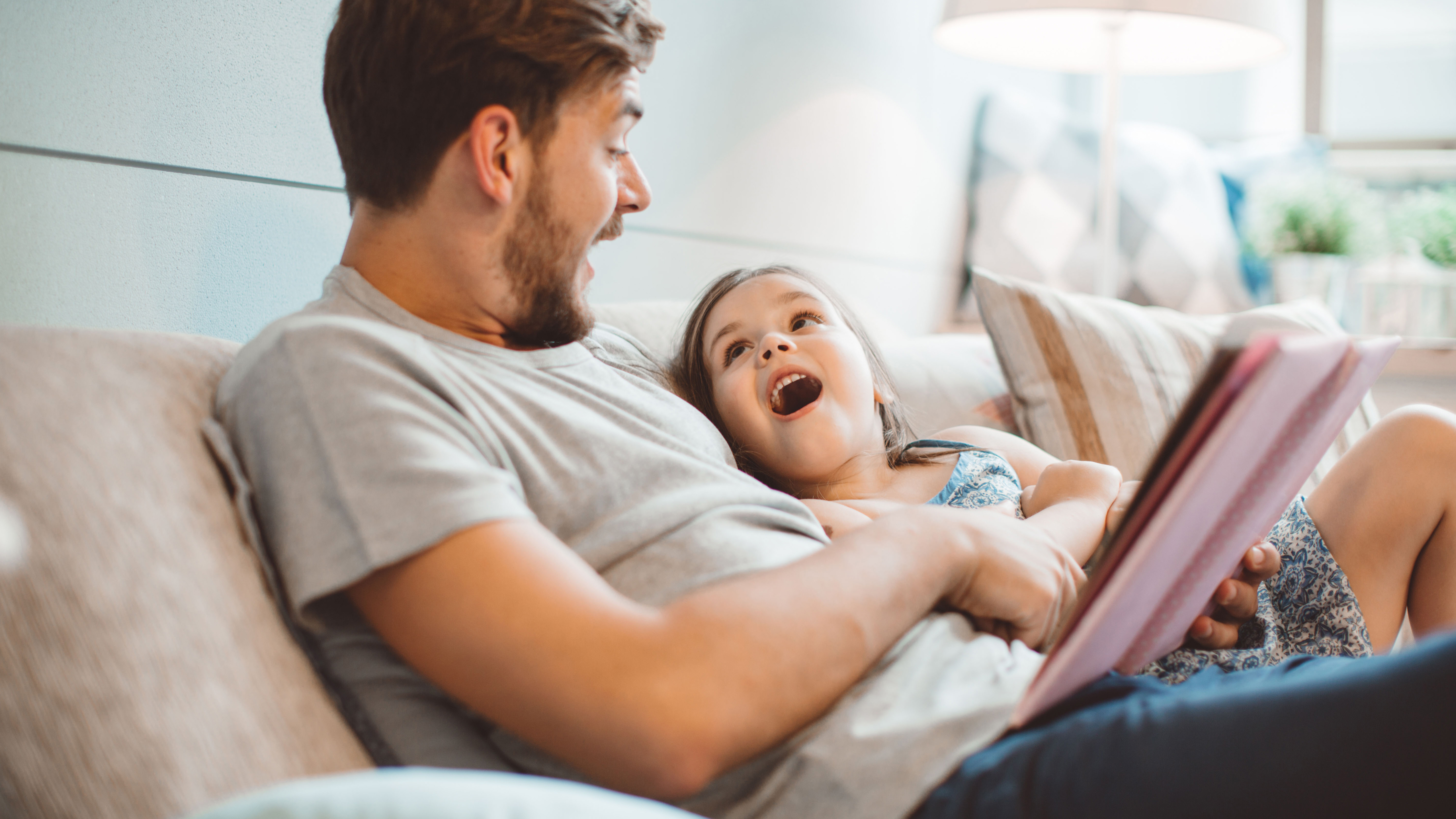 Vater surft mit Tochter im Internet auf dem Tablet und sitzen dabei auf einem Sofa.