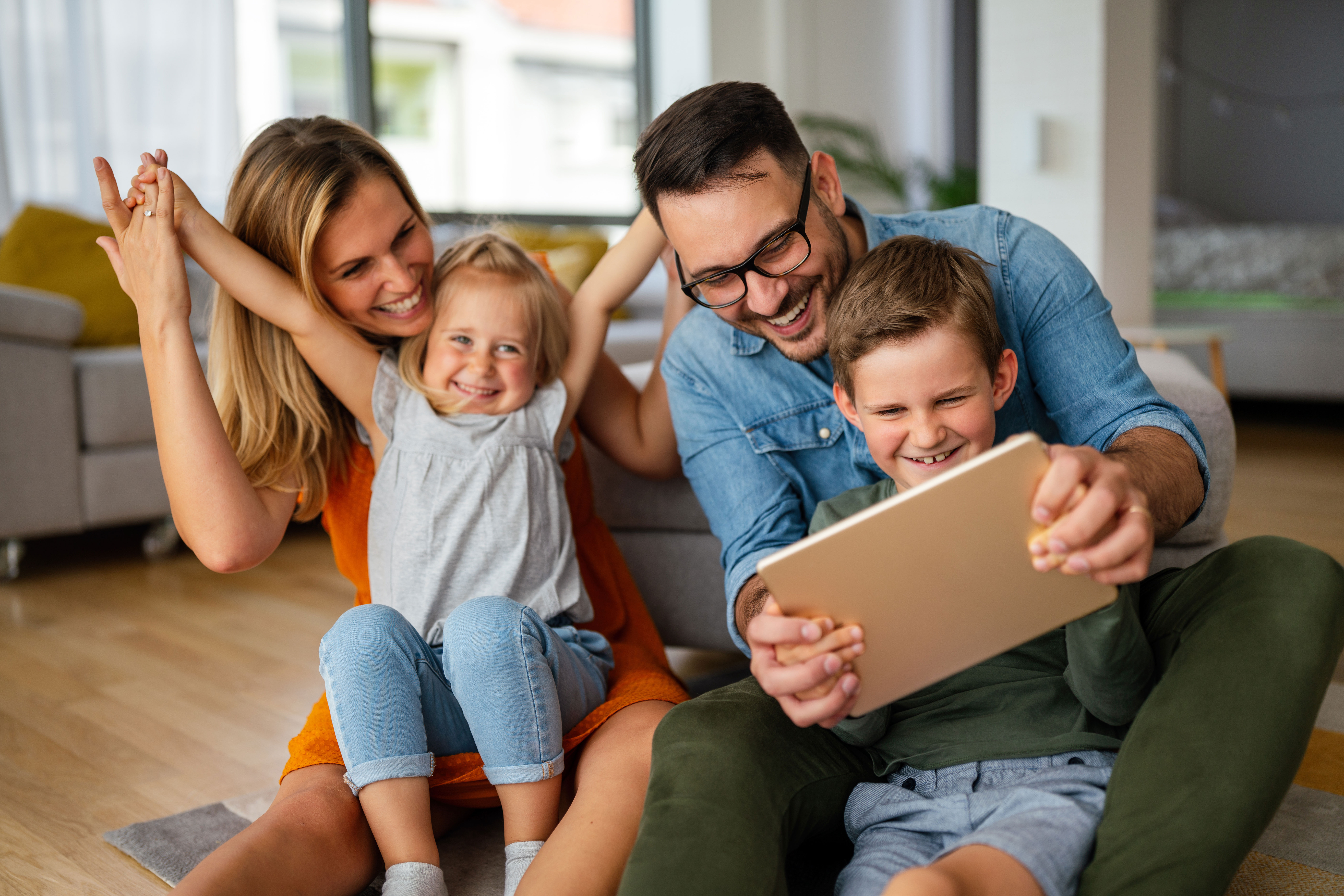 Die Eltern spielen zusammen mit ihren Kindern auf dem Boden. Sie freuen sich über günstige Tarife der NEW Energie. 