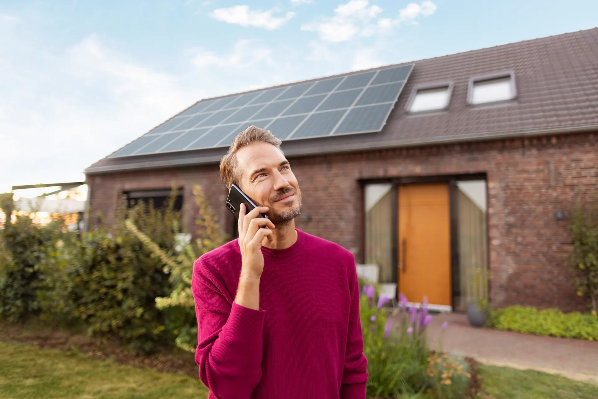 Telefonat über Photovoltaikanlagen Ein Mann telefoniert im Garten vor seinem Haus, mit einer Photovoltaik Anlage von der NEW Energie auf dem Dach.