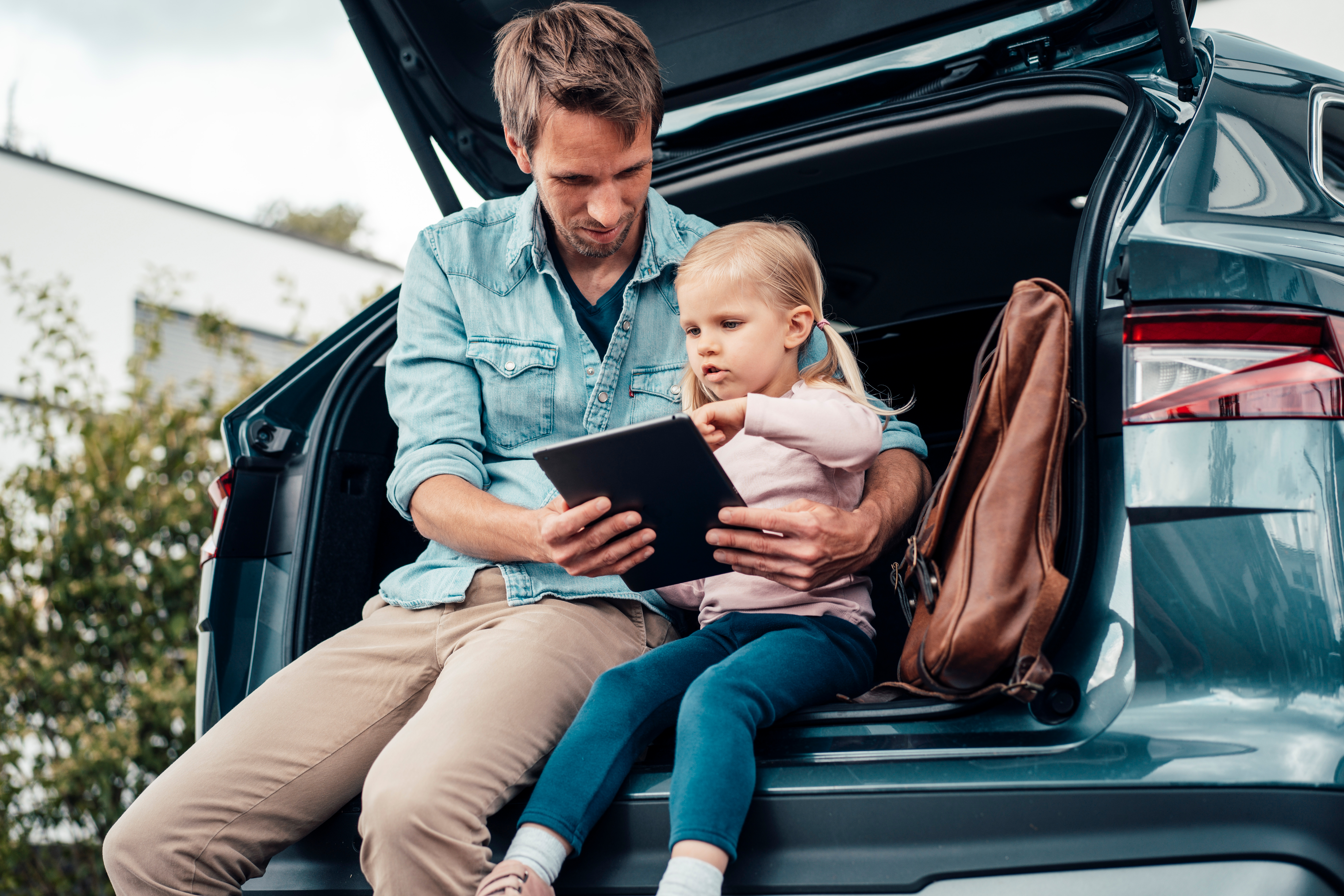 Vater und Tochter sitzen im offenen Kofferraum und vergleichen die Autostromtarife der NEW Energie über ein Tablet.