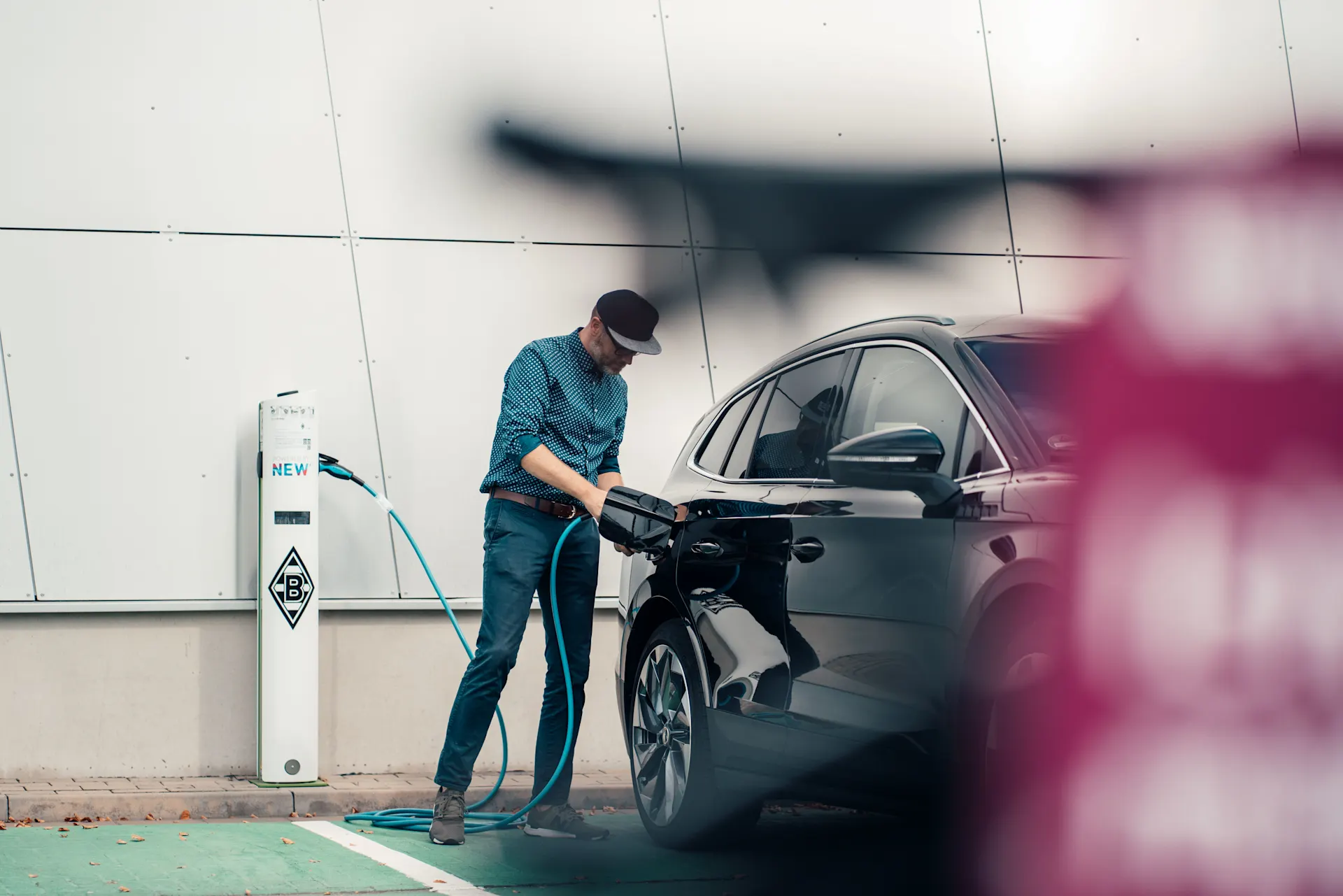 E-Auto wird mit einem Ladekabel an die Wallbox gestellt Der Mann lädt auf einem öffentlichen Parkplatz das E-Auto über eine Wallbox auf.